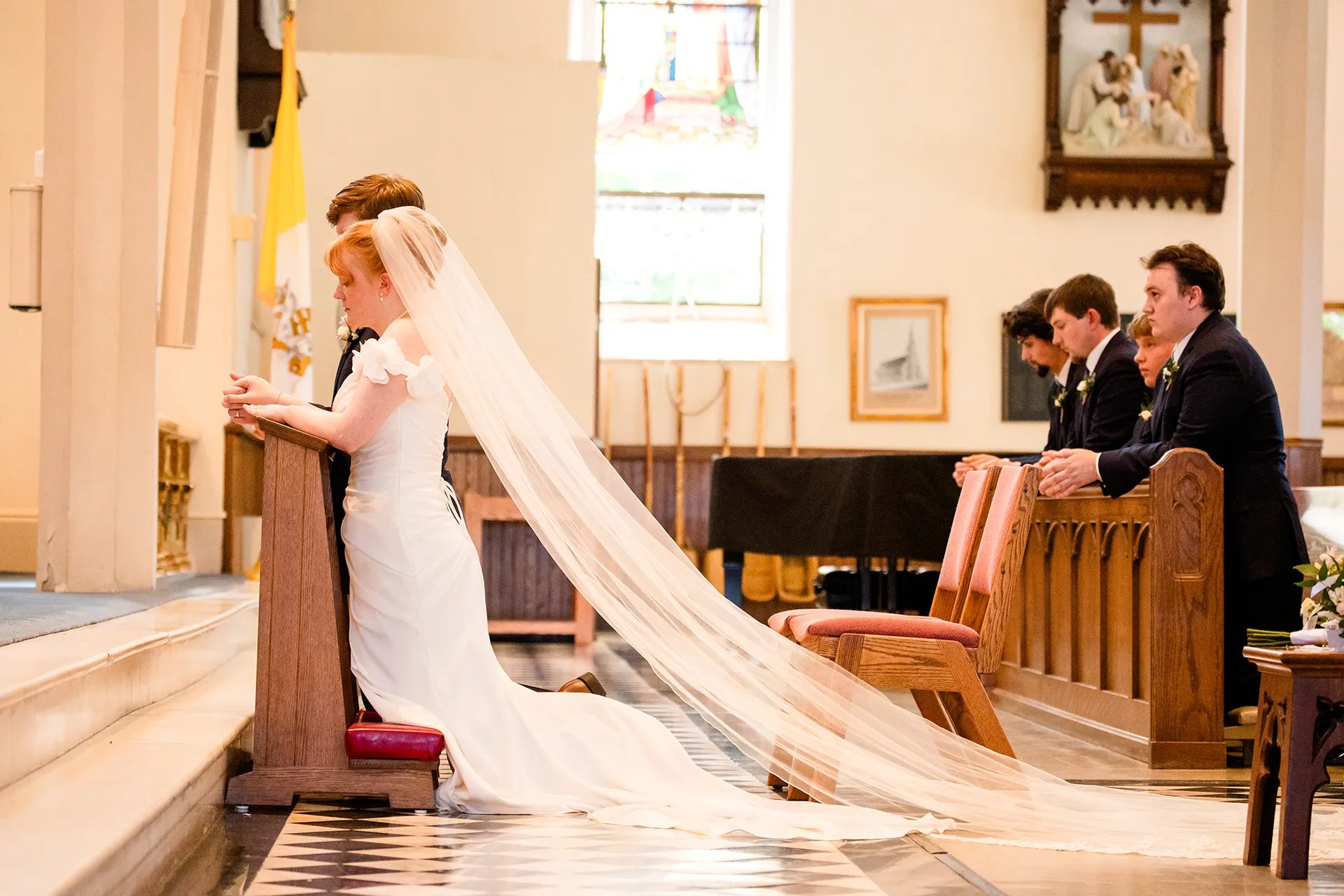 A bride and groom kneel at the head of the aisle during a catholic wedding ceremony at Saint John's Catholic Church in Bangor, Maine.
