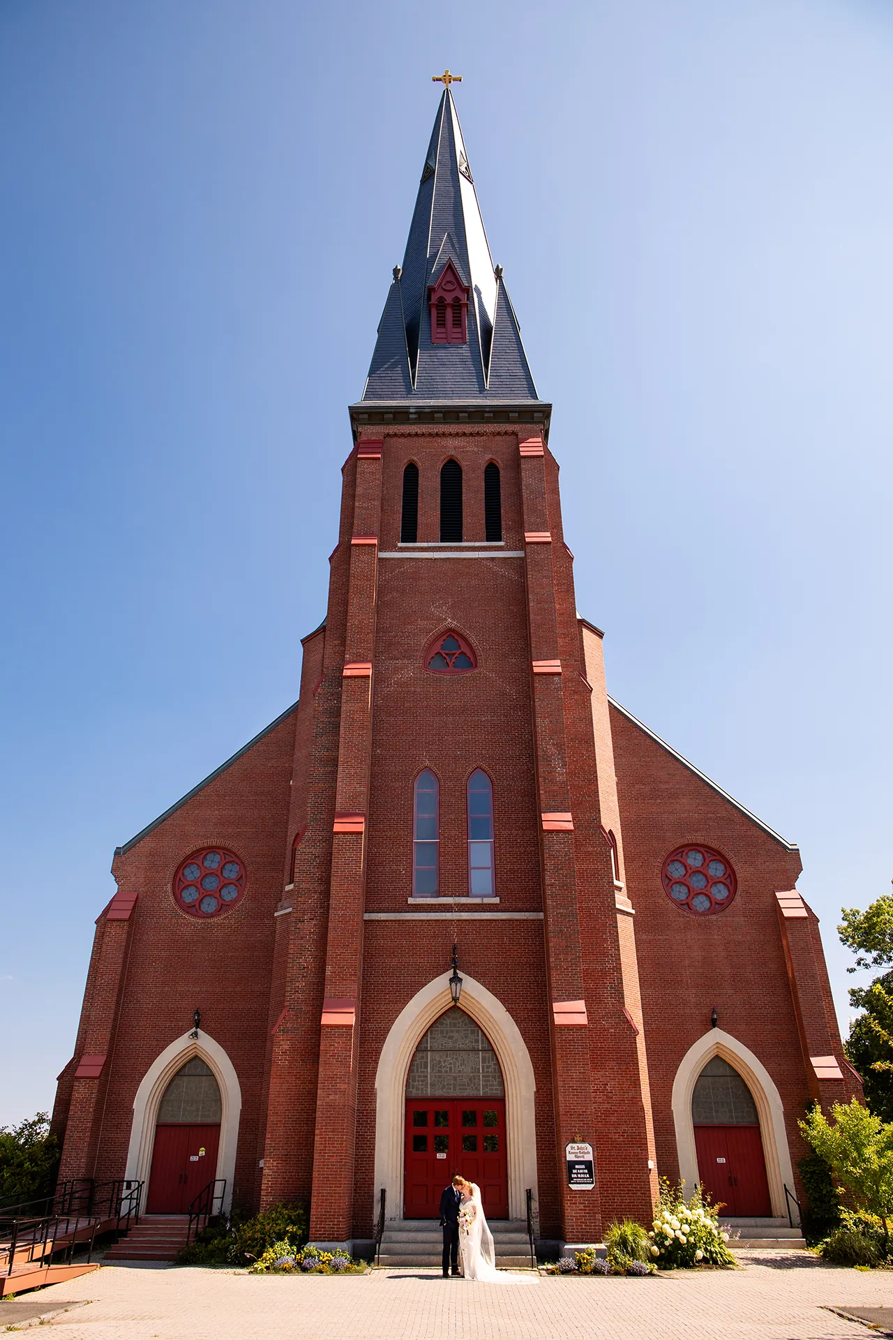 A bride and groom kiss in front of Saint John's Catholic Church in Bangor, Maine during wedding portraits.