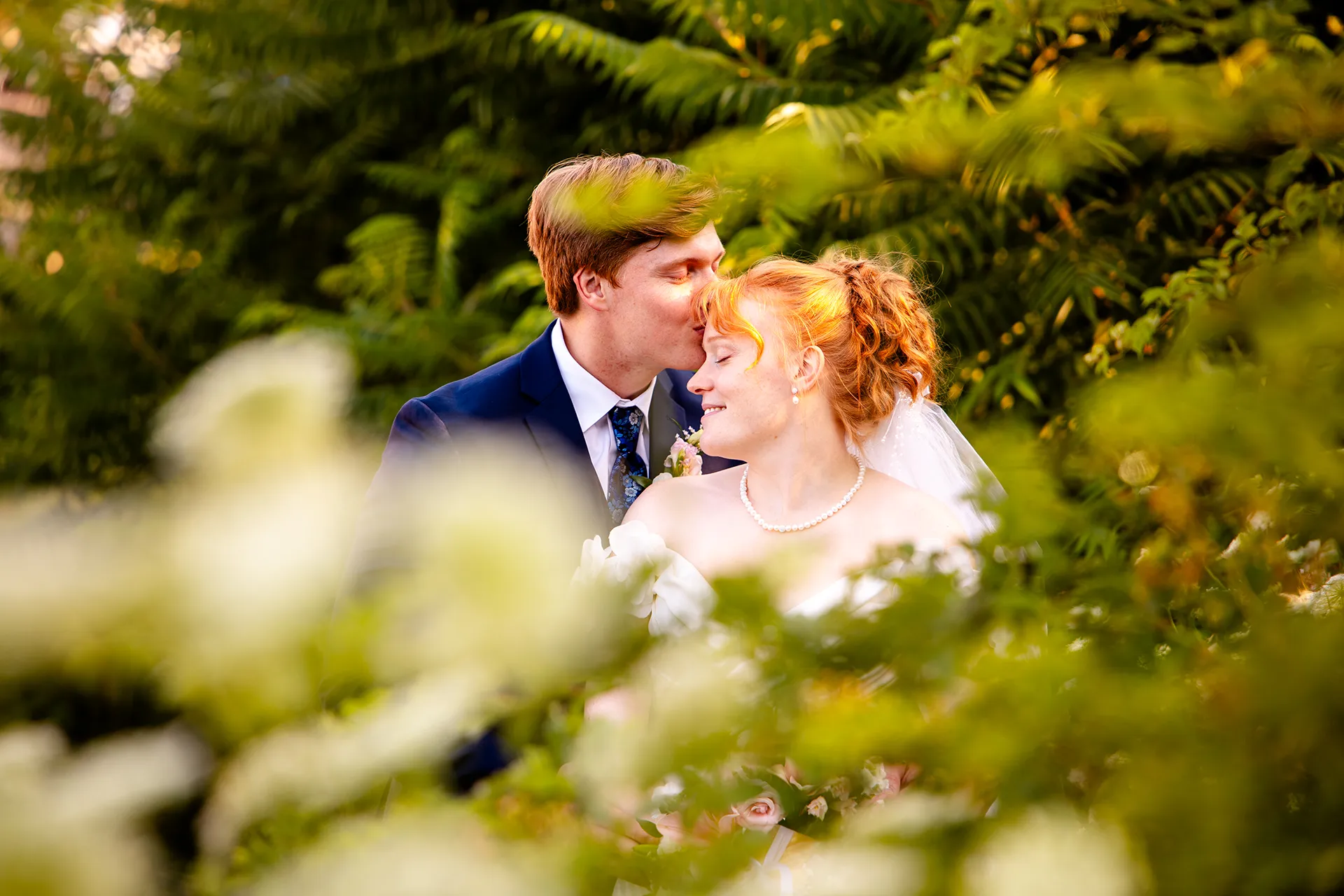 A bride smiles as a groom kisses her on the head during wedding portraits at the Hilton Garden Inn in Bangor, Maine.