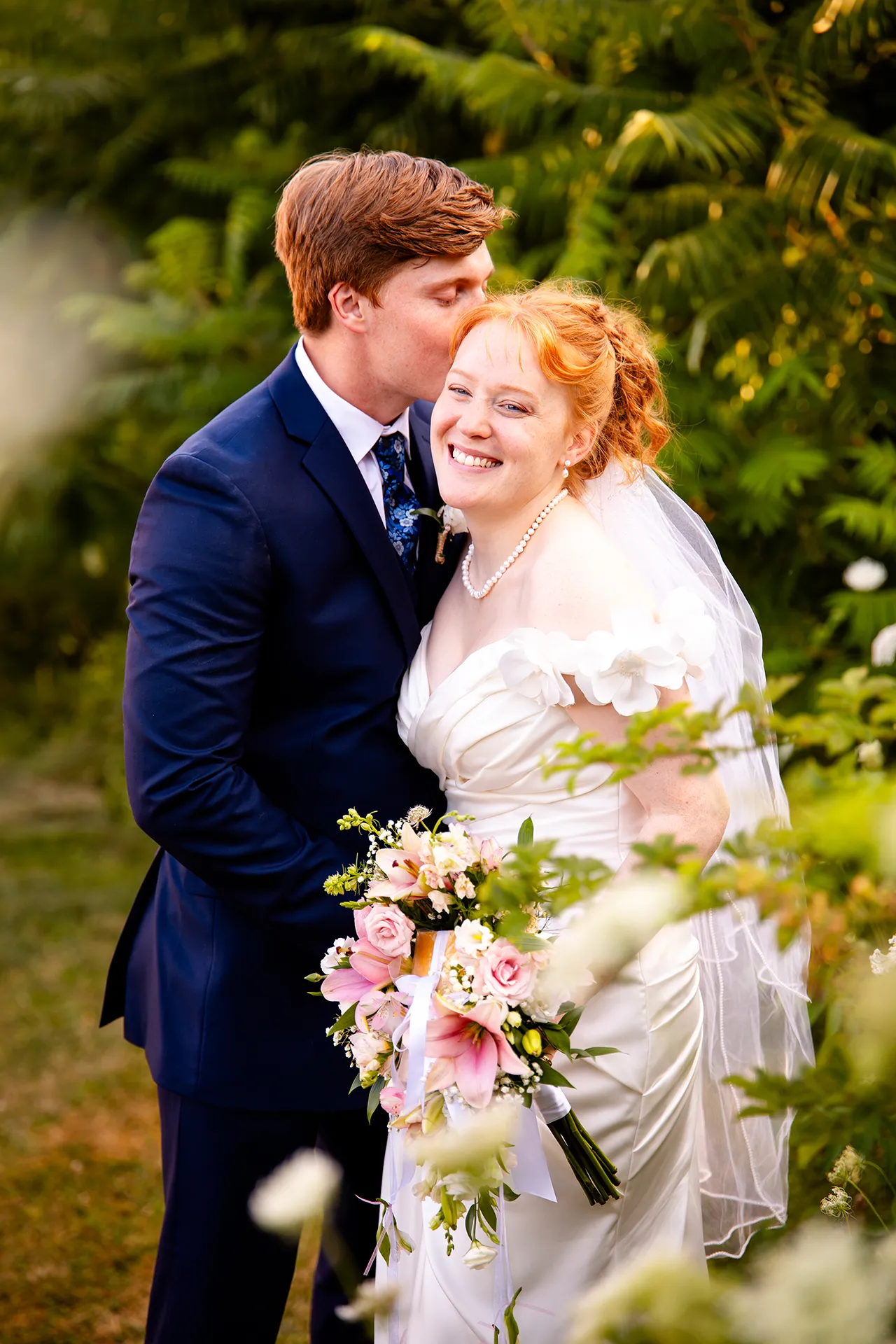 A bride laughs as a groom kisses her on the head during wedding portraits at the Hilton Garden Inn in Bangor, Maine.