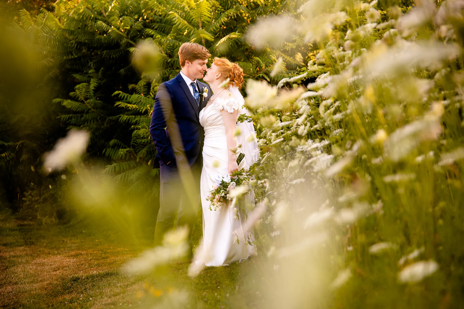 A newly married couple stand behind flowers and rubbing noses during wedding portraits at the Hilton Garden Inn in Bangor, Maine.