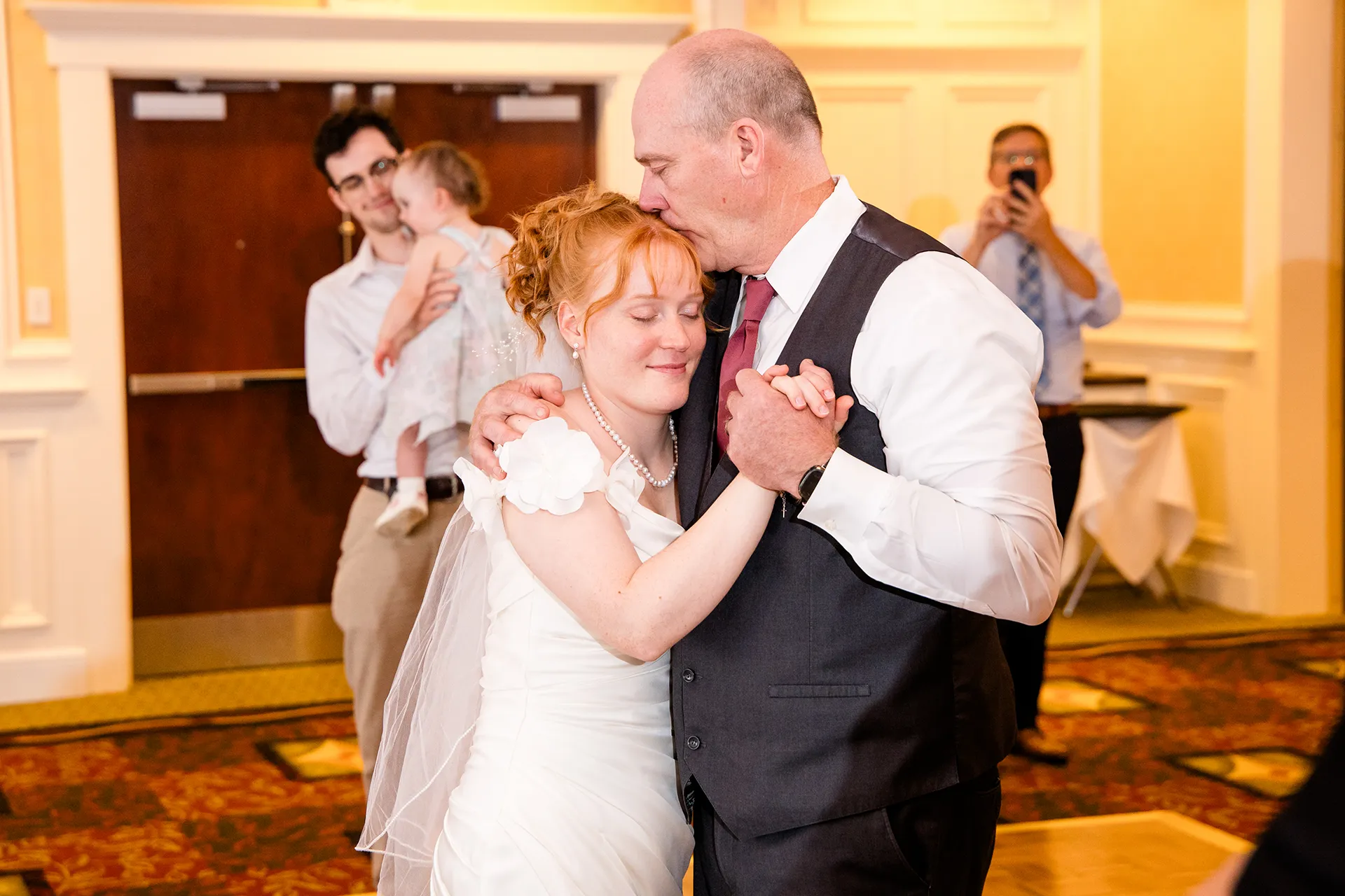 A dad kisses a bride on the head during a dance at a wedding reception at Hilton Garden Inn in Bangor, Maine.