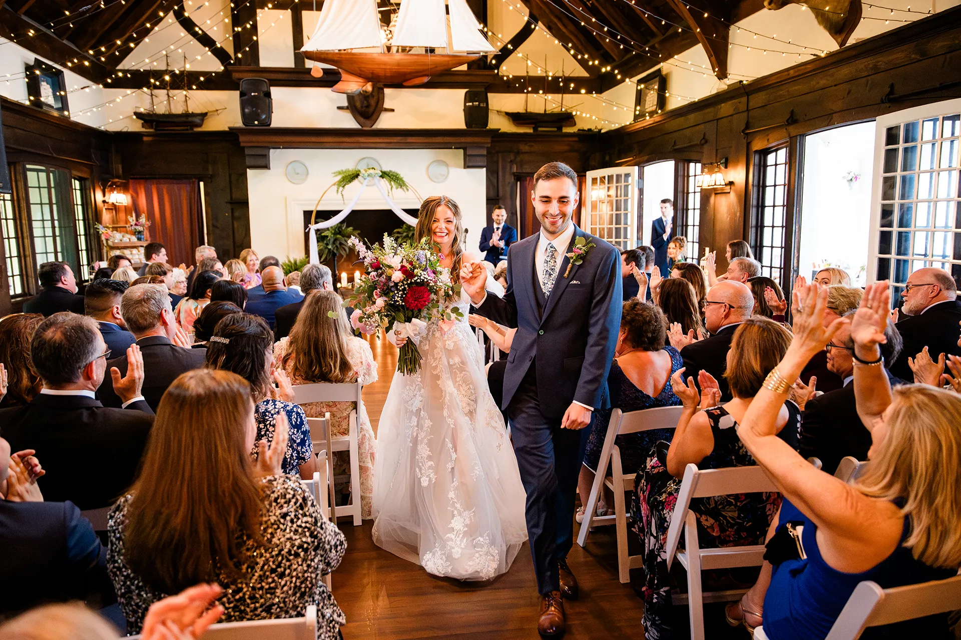 maine wedding photography bethany mike 35 A newly married couple hold hands and smile as they walk down the aisle during a wedding ceremony at York Harbor Reading Room in York, Maine.