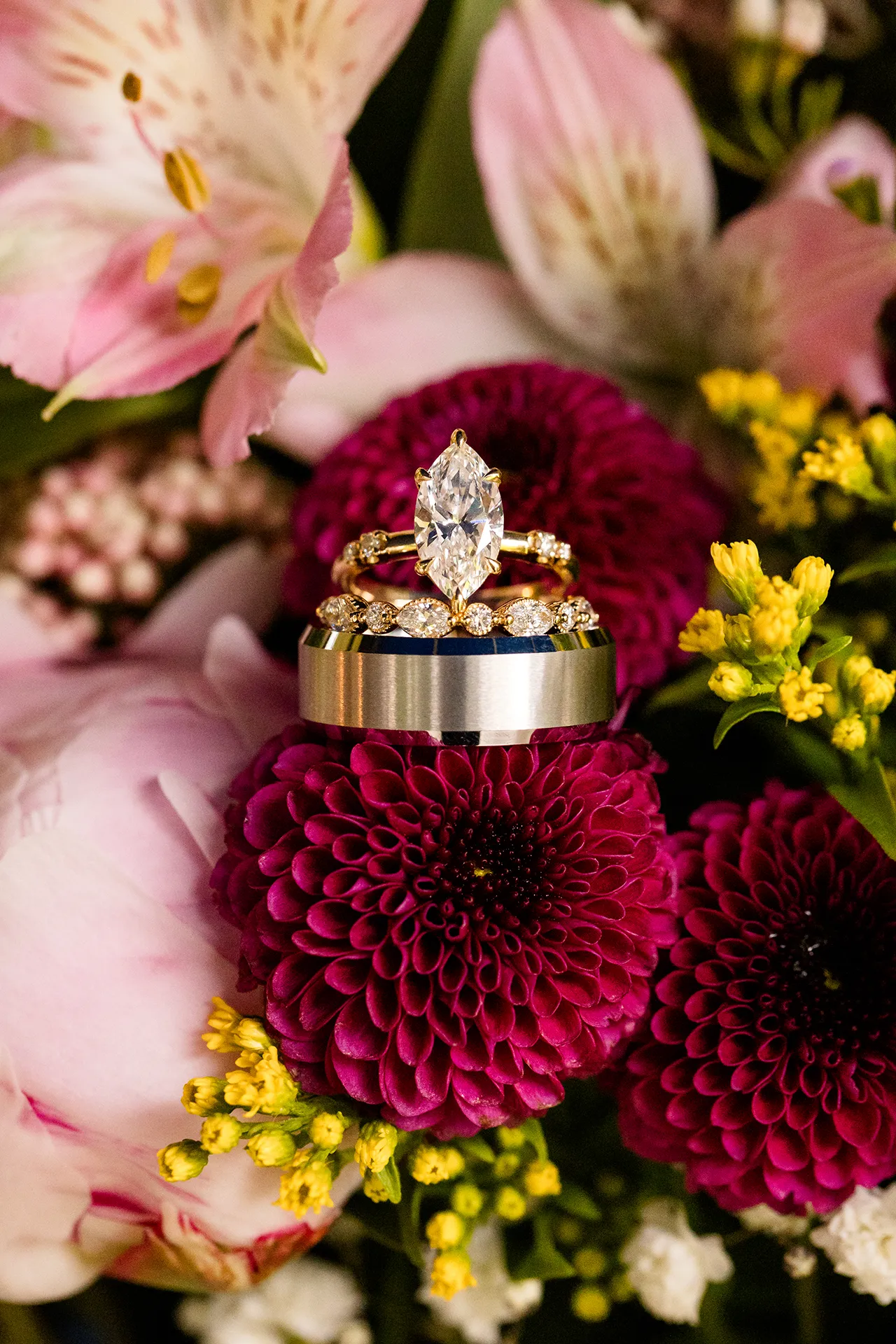maine wedding photography bethany mike 40 A closeup of an engagement ring sitting on top of two wedding rings in a colorful bouquet of flowers at the York Harbor Reading Room in York, Maine.