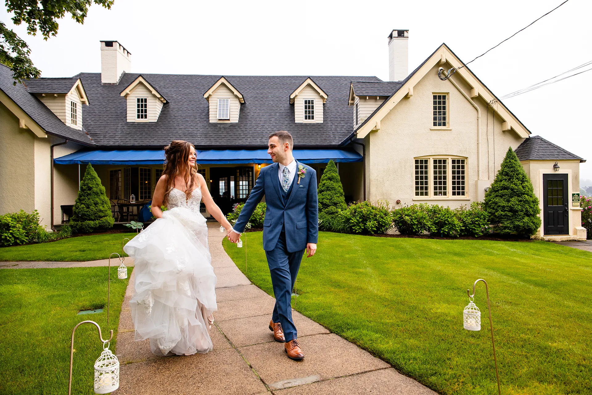 maine wedding photography bethany mike 41 A bride and groom hold hands as they walk along a path in front of the York Harbor Reading Room in York, Maine.
