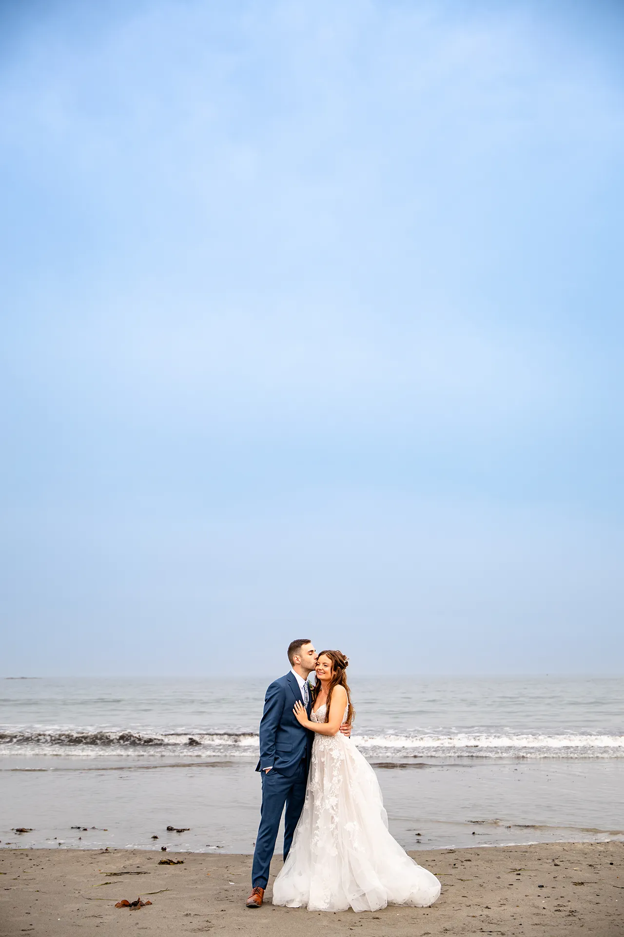maine wedding photography bethany mike 50 A bride smiles as a groom kisses her on the cheek during wedding portraits on York Harbor Beach in York, Maine.