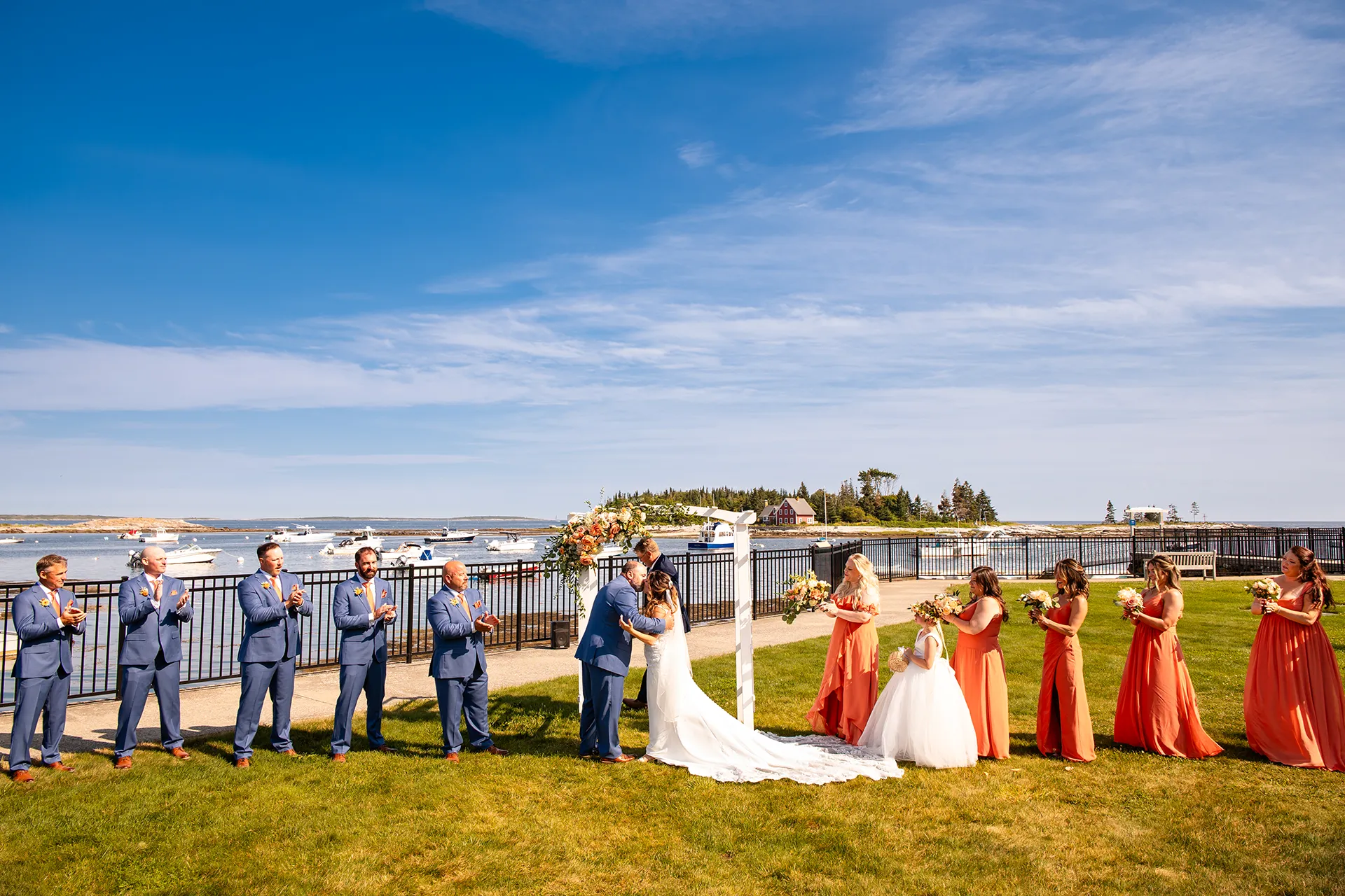 A bride and groom kiss while their wedding party claps during a wedding ceremony at the Newagen Seaside Inn in Southport Maine.