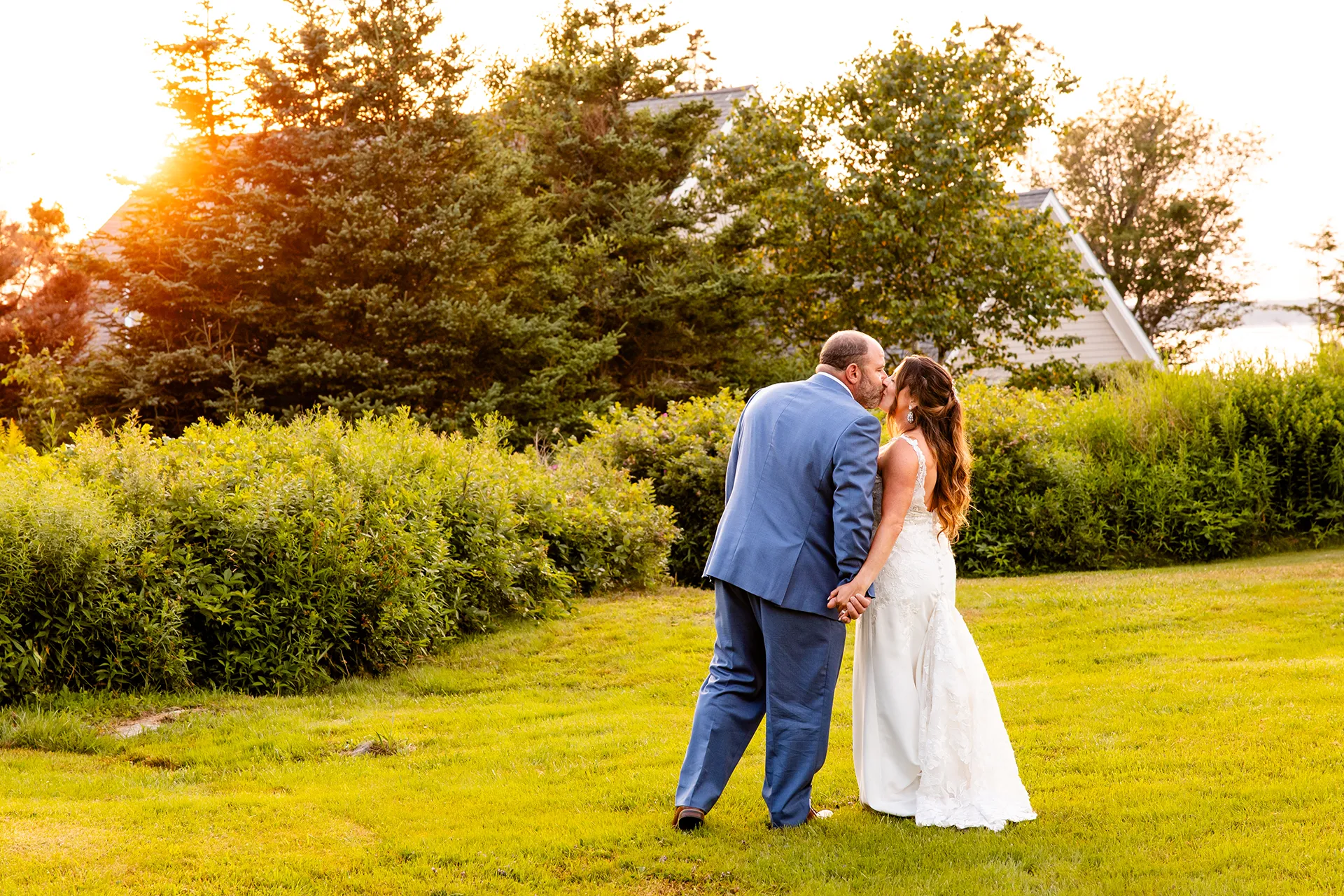 A bride and groom hold hands and kiss in a field during wedding portraits at the Newagen Seaside Inn in Southport Maine.