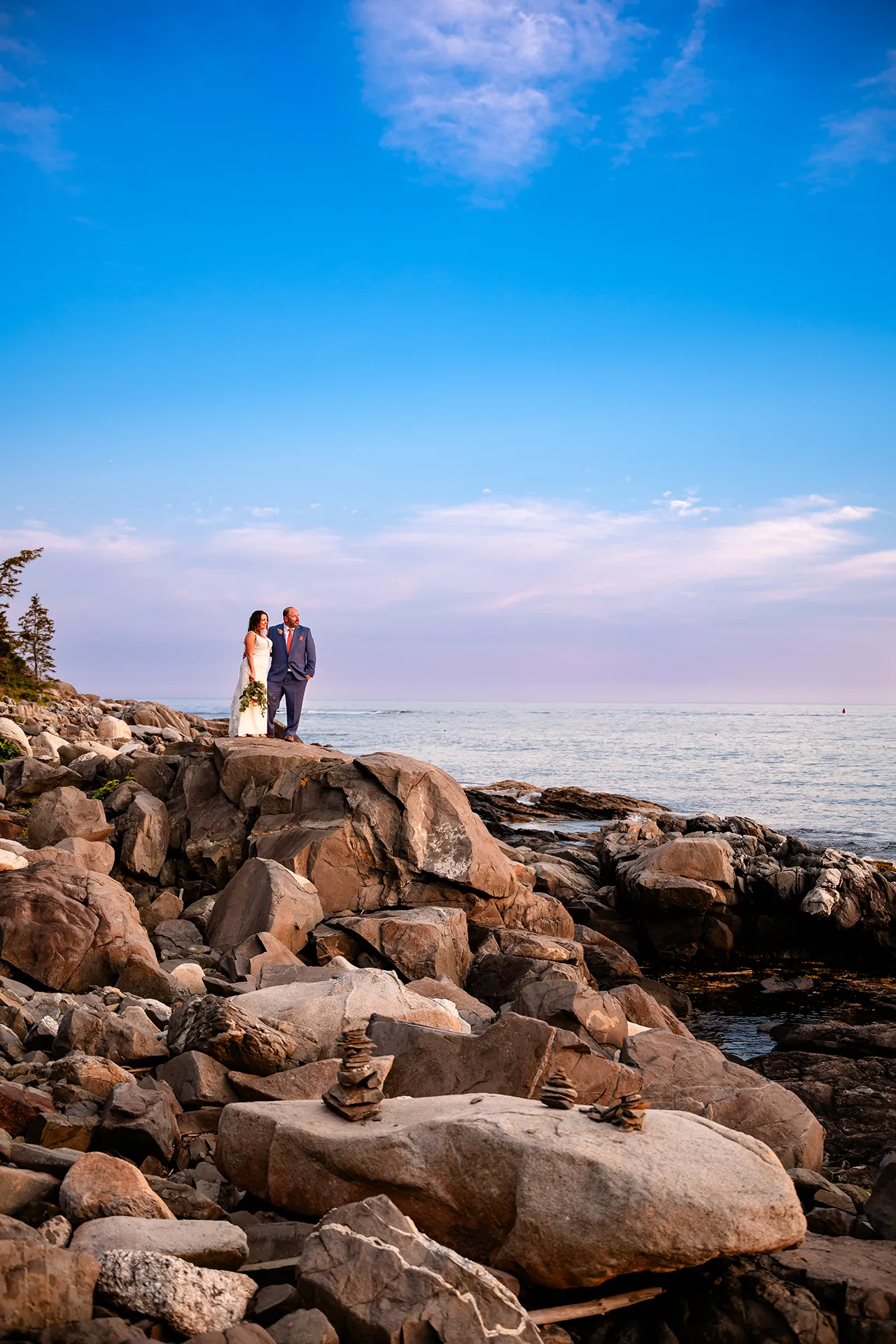A bride and groom stand on a cliff at sunset as they pose for their wedding portraits at the Newagen Seaside Inn in Southport Maine.