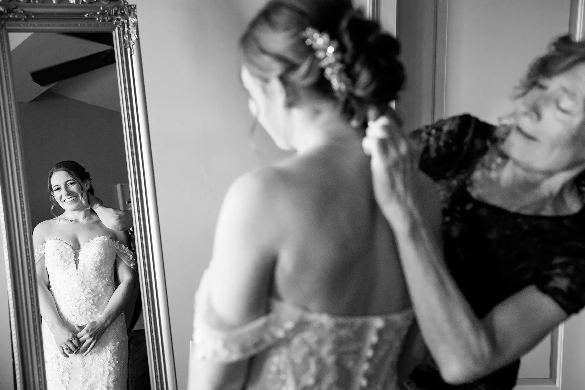 A brides looks at herself in the mirror as her mom puts on her necklace at the Atlantic Oceanside Hotel & Event Center in Bar Harbor, Maine.
