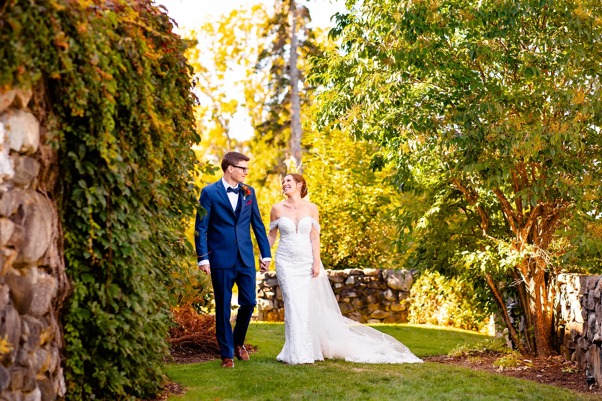 A bride and groom hold hands and walk in the side garden at the Willows on the property of the Atlantic Oceanside Hotel & Event Center in Bar Harbor.