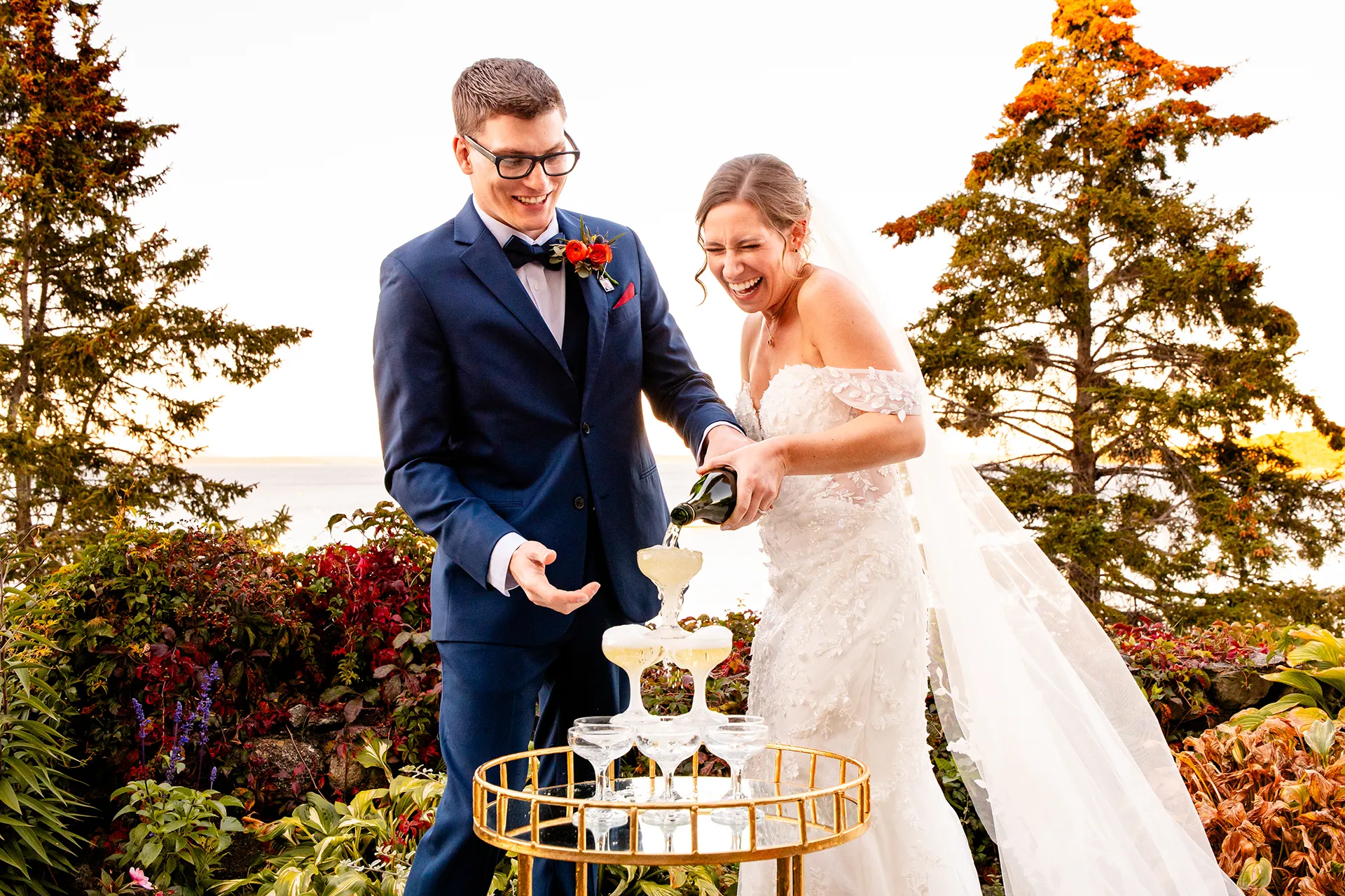 A bride and groom laugh as they pour champagne into glasses at the Atlantic Oceanside Hotel & Event Center in Bar Harbor, Maine.
