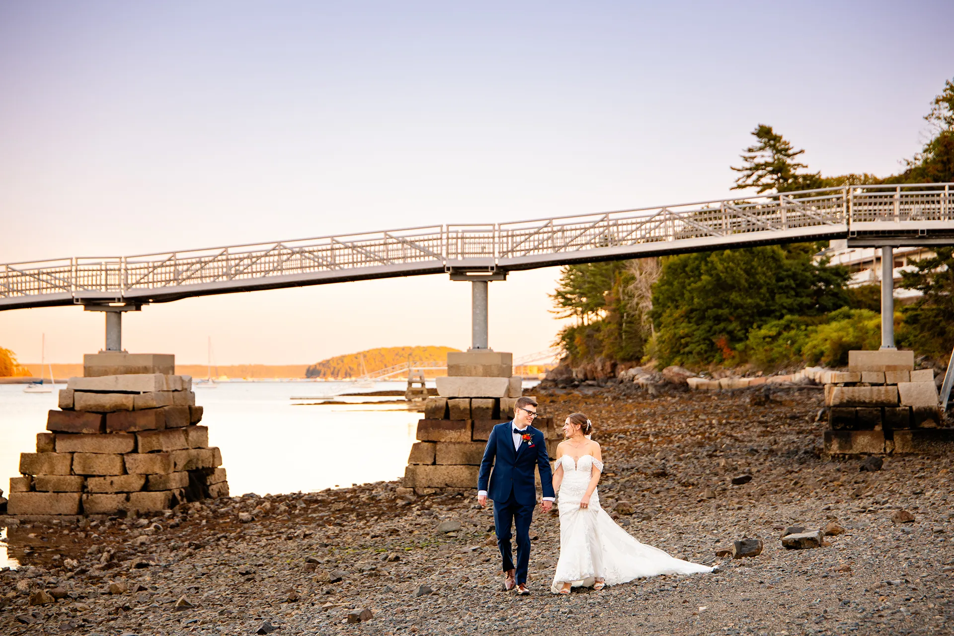 A newly married couple hold hands and walk on the rocky beach at the Atlantic Oceanside Hotel & Event Center in Bar Harbor, Maine.