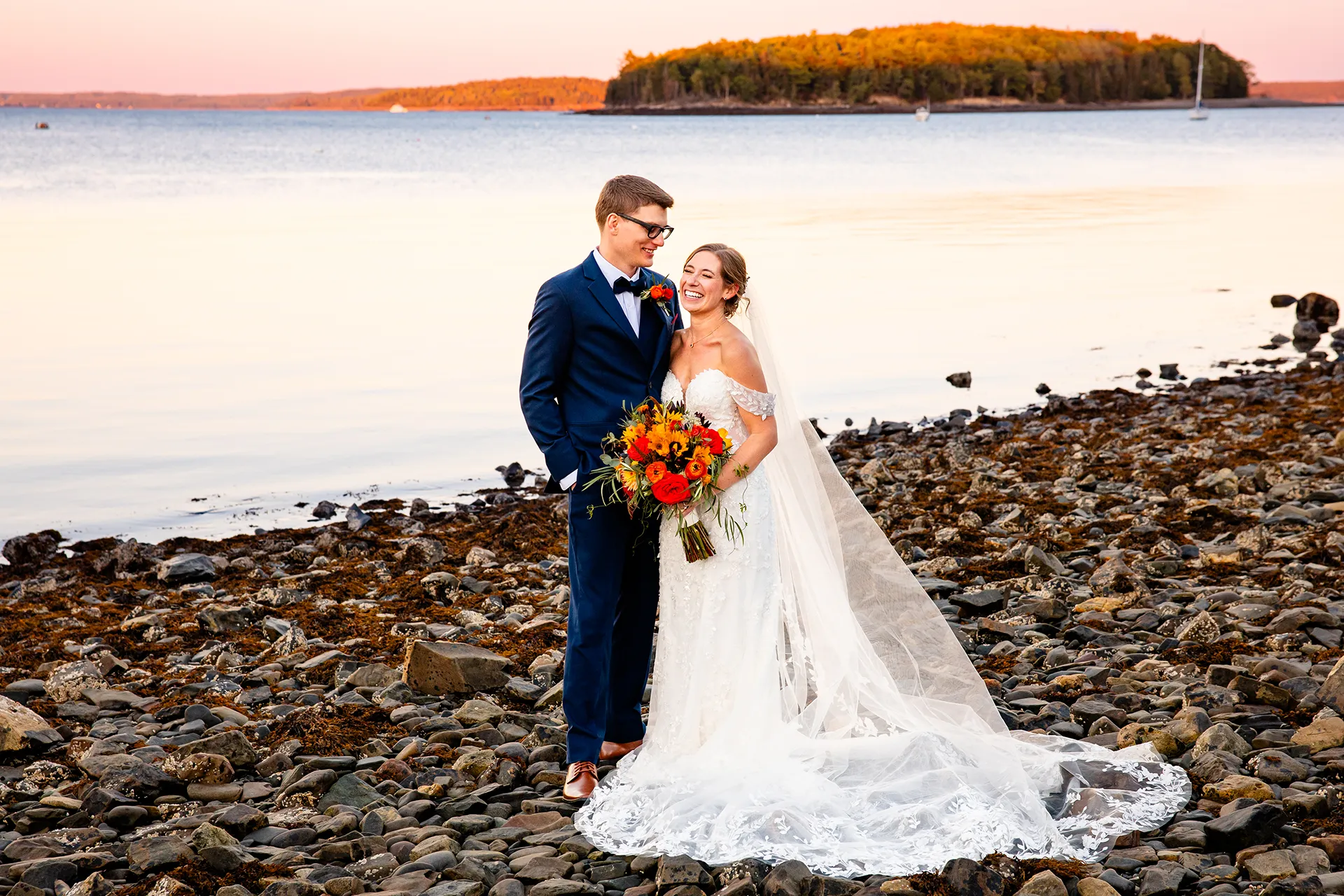 A bride and groom laugh as they pose for wedding portraits on a beach at the Atlantic Oceanside Hotel & Event Center in Bar Harbor, Maine.
