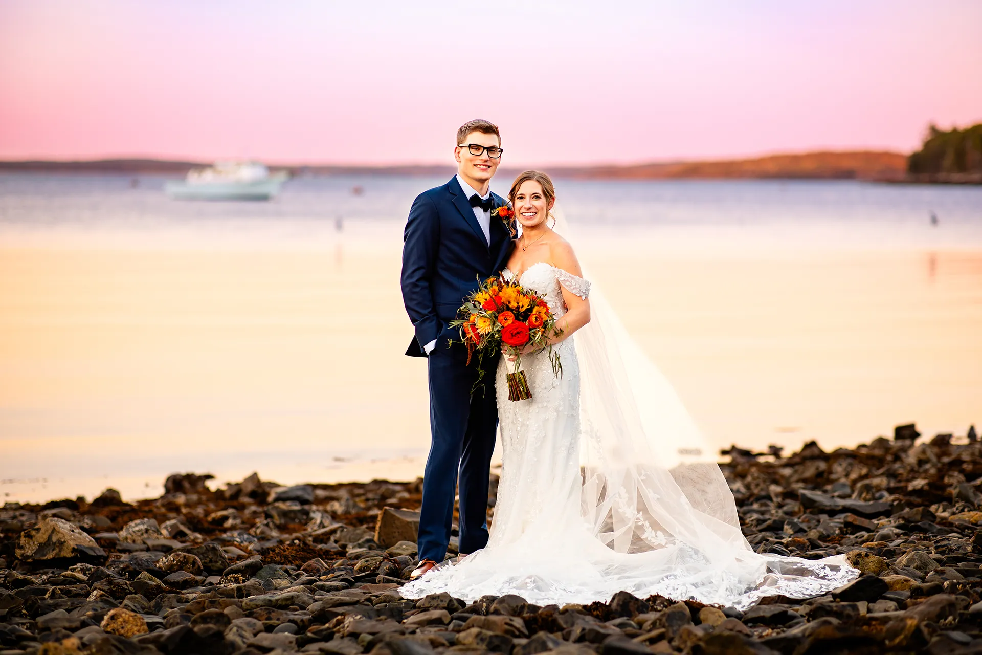 A bride and groom smile and pose for sunset wedding portraits on a beach at the Atlantic Oceanside Hotel & Event Center in Bar Harbor, Maine.