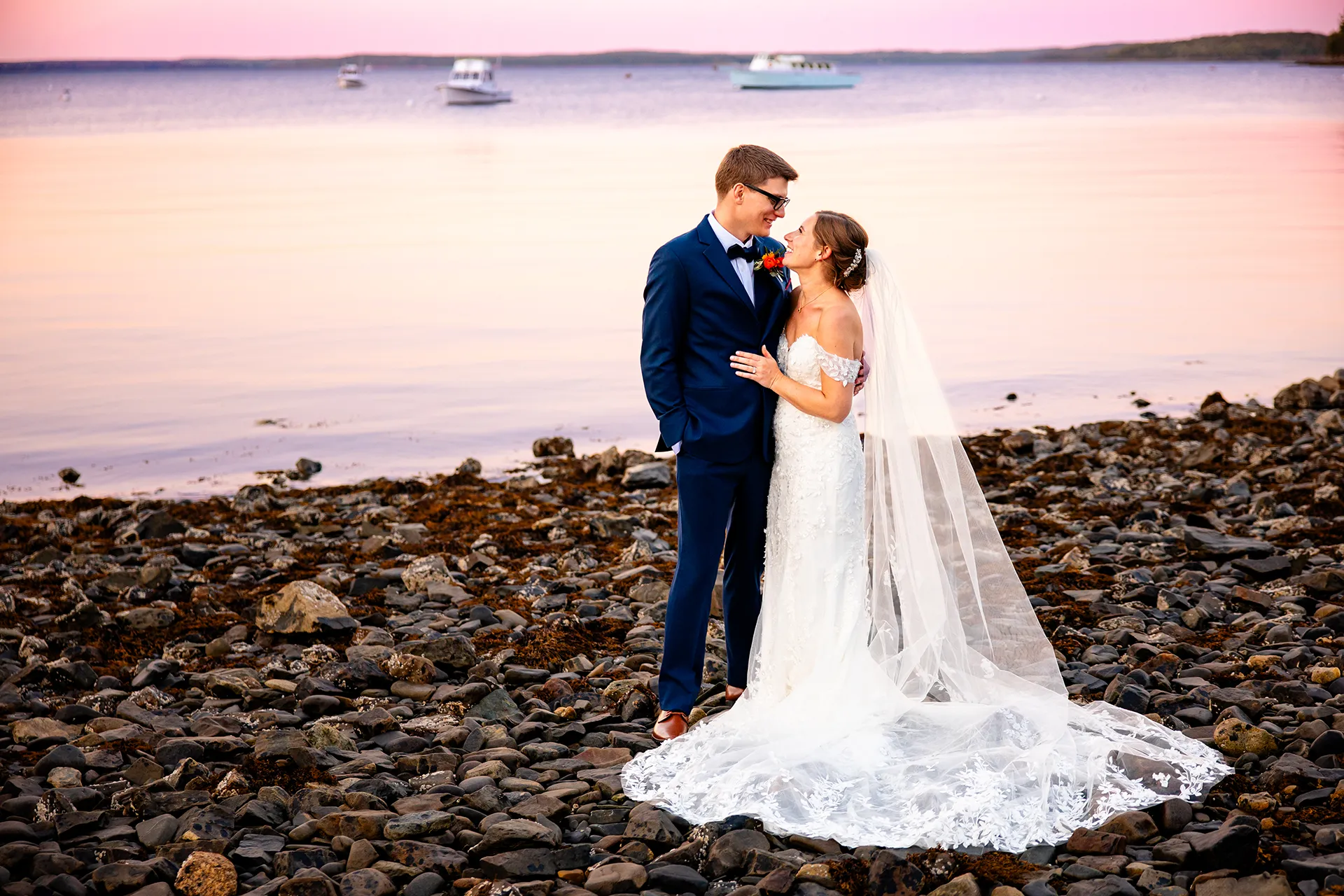 A bride and groom smile at each other during sunset wedding portraits on a beach at the Atlantic Oceanside Hotel & Event Center in Bar Harbor, Maine.