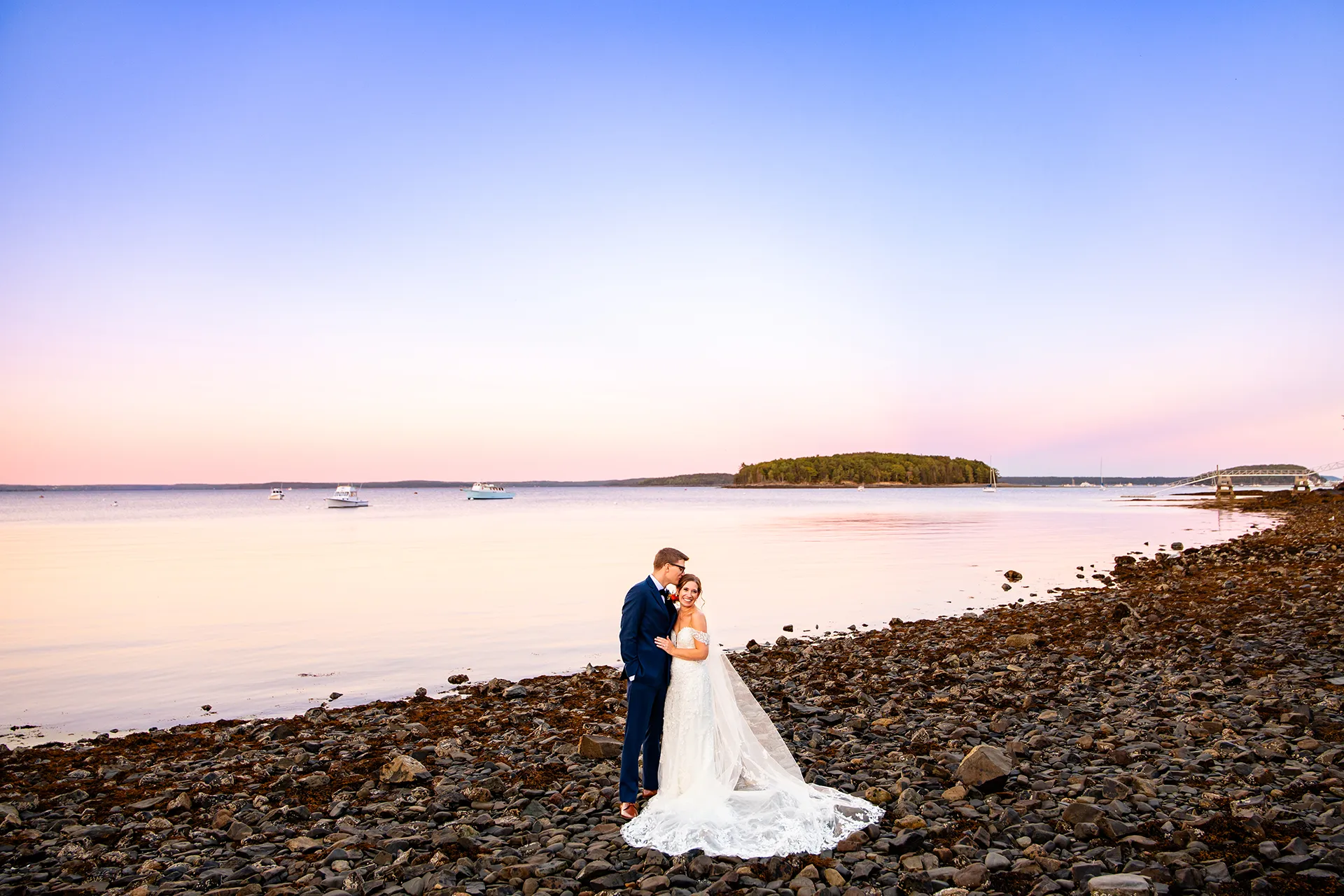 A groom kisses a bride on the head during sunset wedding portraits on a beach at the Atlantic Oceanside Hotel & Event Center in Bar Harbor, Maine.