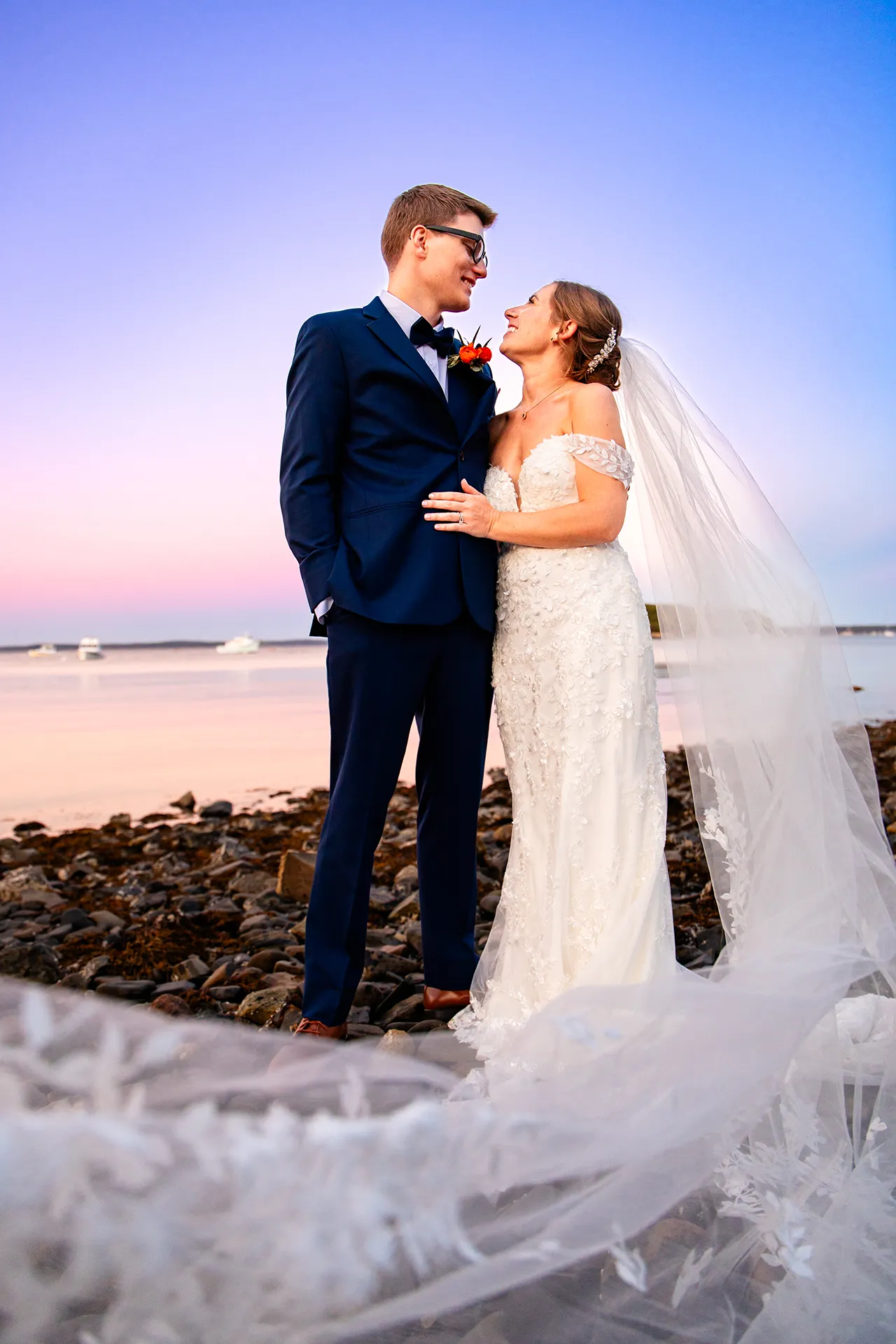 A bride and groom smile at each other during sunset wedding portraits on a beach at the Atlantic Oceanside Hotel & Event Center in Bar Harbor, Maine.