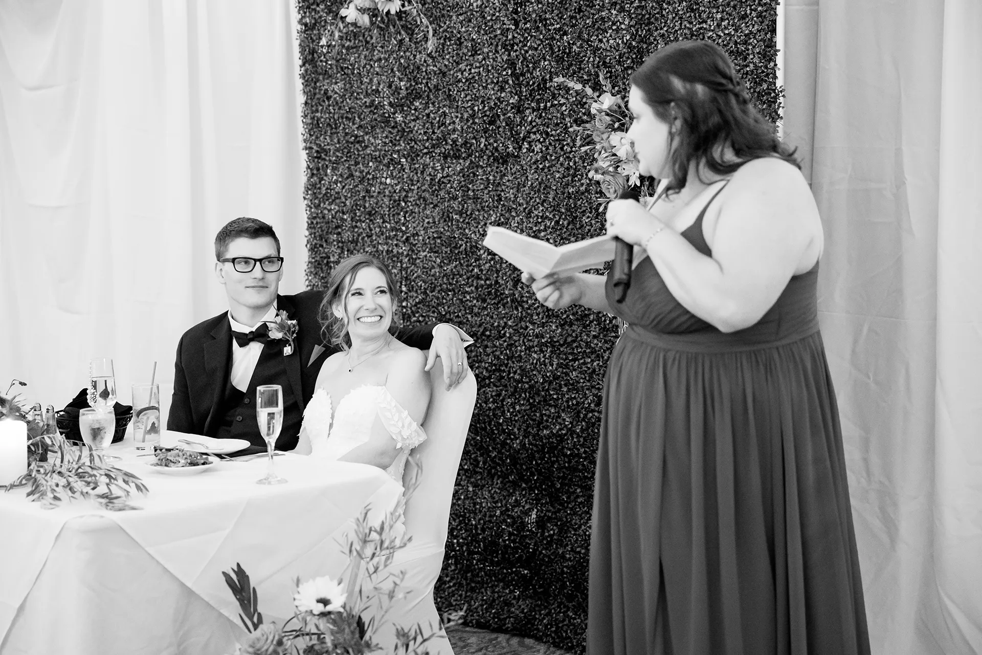 A bride and groom smile as they listen to a bridesmaid give a toast during a reception at the Atlantic Oceanside Hotel & Event Center in Bar Harbor, Maine.