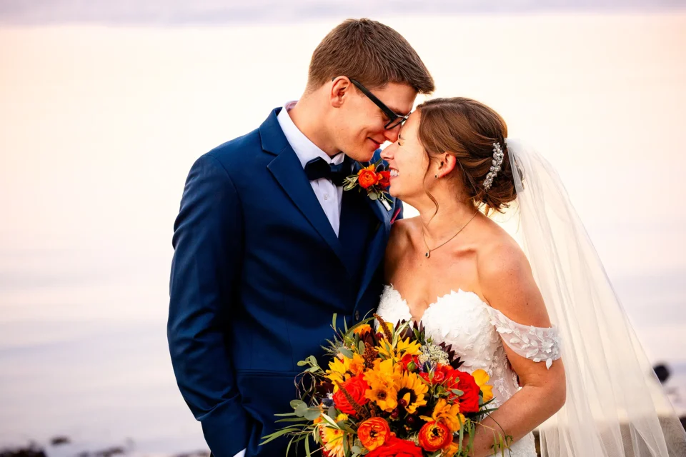 A bride and groom smile as they snuggle together during wedding portraits at the Atlantic Oceanside Hotel & Event Center in Bar Harbor, Maine.