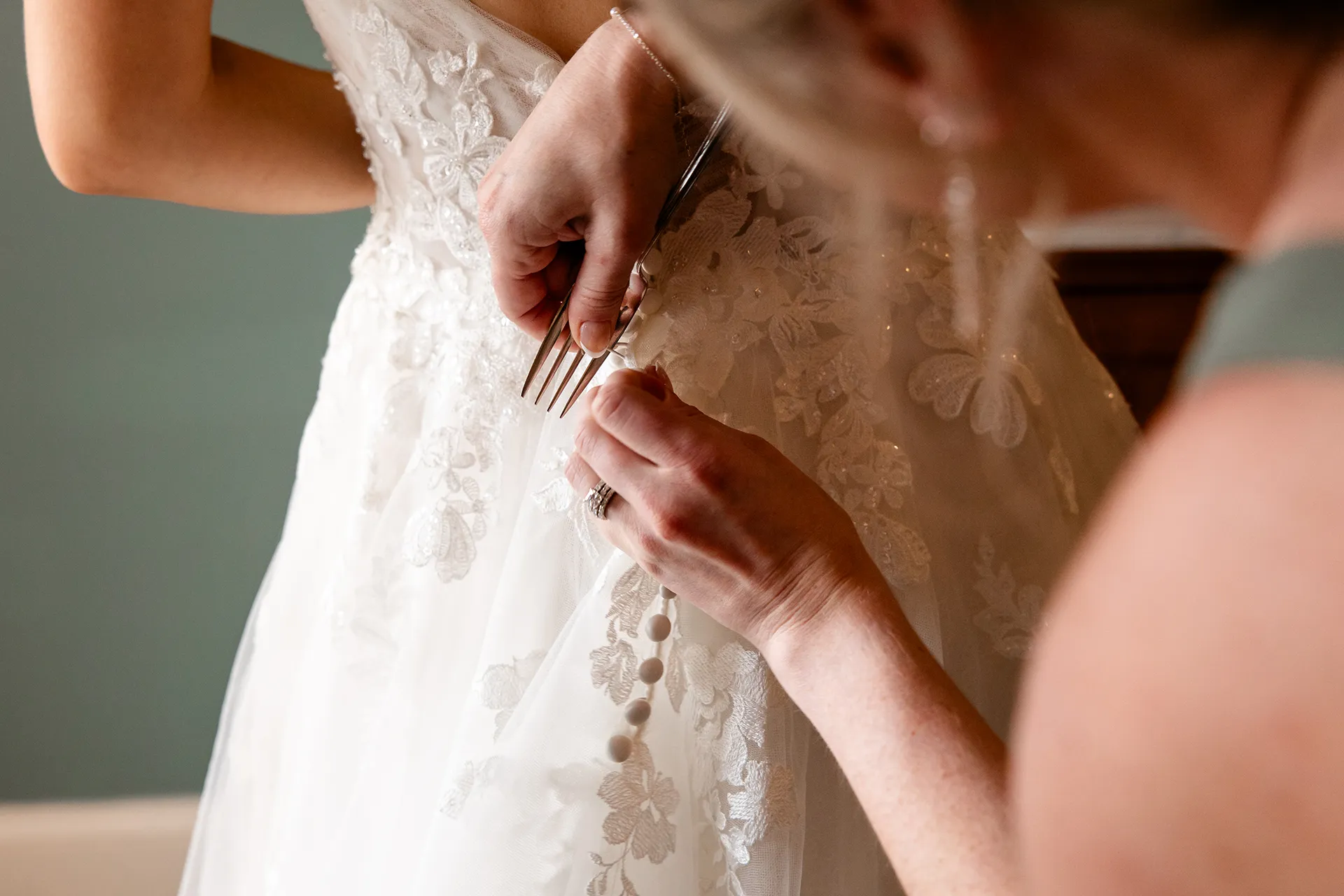 A closeup of a bridesmaid using a fork to button up the bride's dress at the Bar Harbor Inn and Spa near Acadia National Park in Maine.