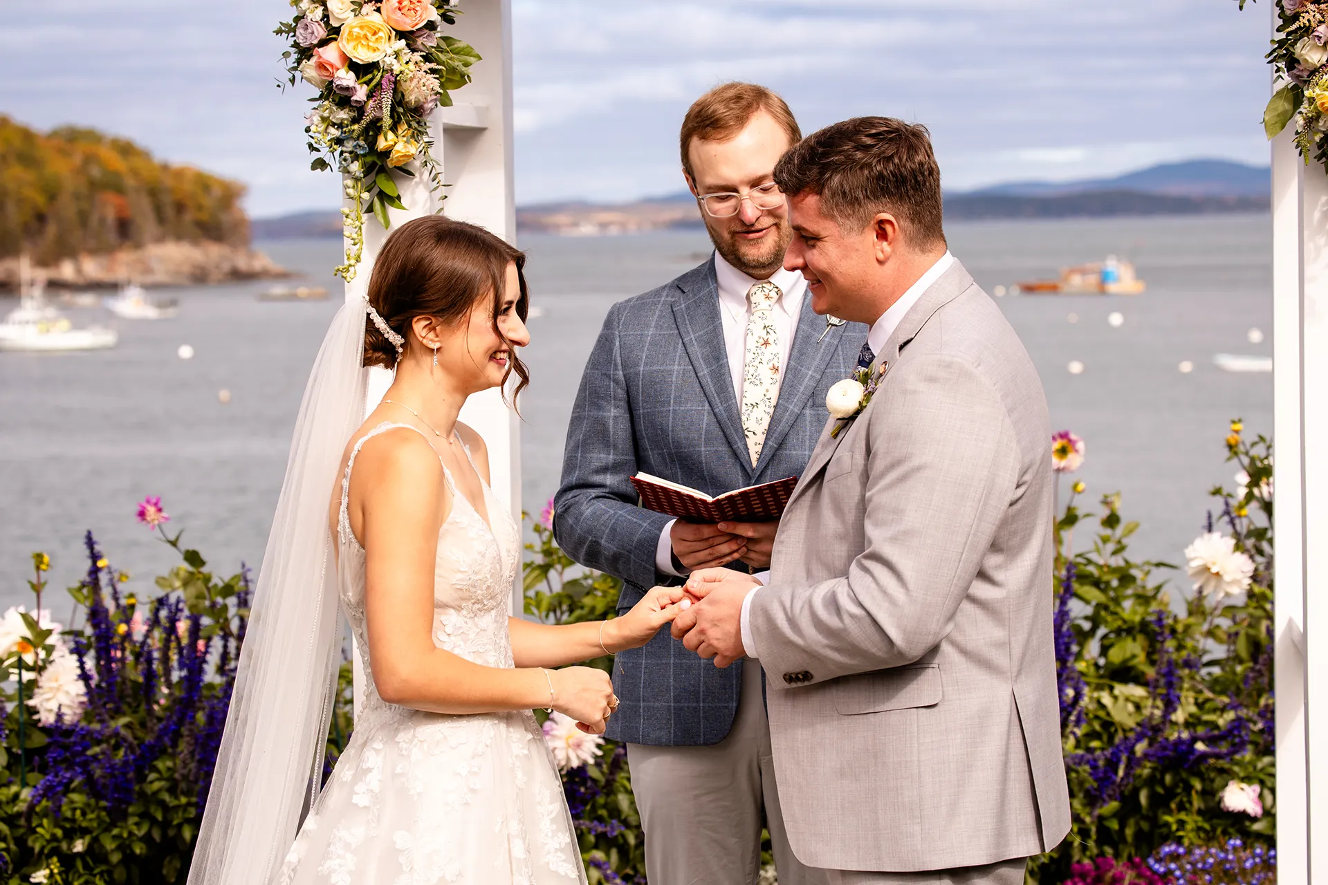 A bride and groom hold hands and smile at each other during a wedding ceremony at the Bar Harbor Inn and Spa near Acadia National Park in Maine.