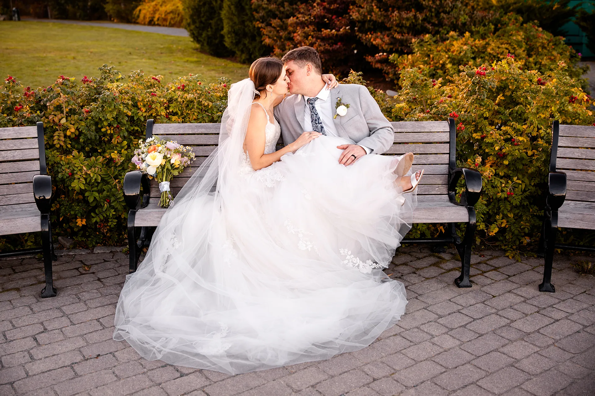 A bride and groom sit on a bench and kiss during wedding portraits on the property of the Bar Harbor Inn near the Acadia National Park in Maine.