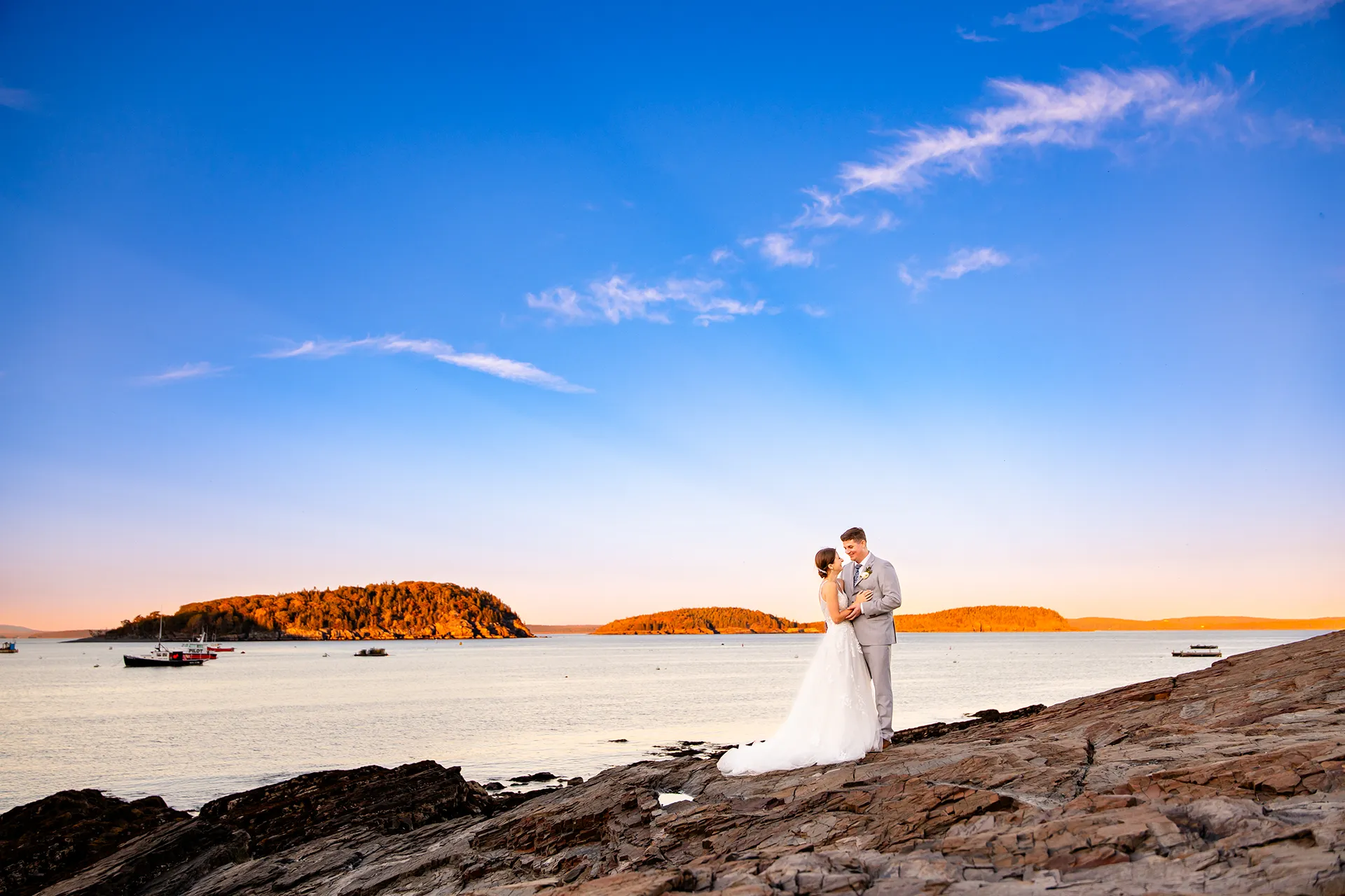 A bride and groom stand on a cliff overlooking Bar Island during wedding portraits at the Bar Harbor Inn near the Acadia National Park in Maine.