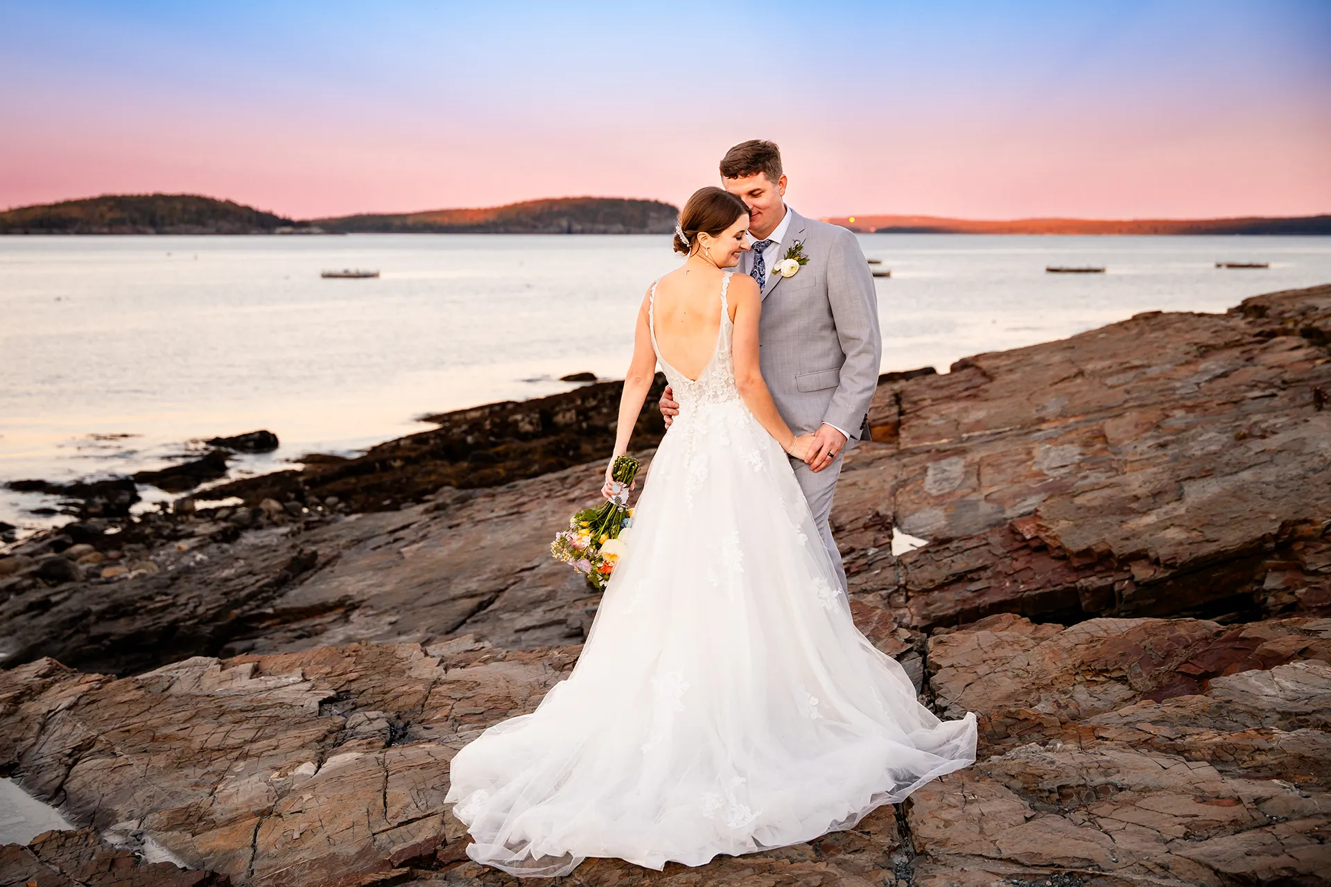 A bride and groom snuggle together during sunset wedding portraits on the property of the Bar Harbor Inn near the Acadia National Park in Maine.