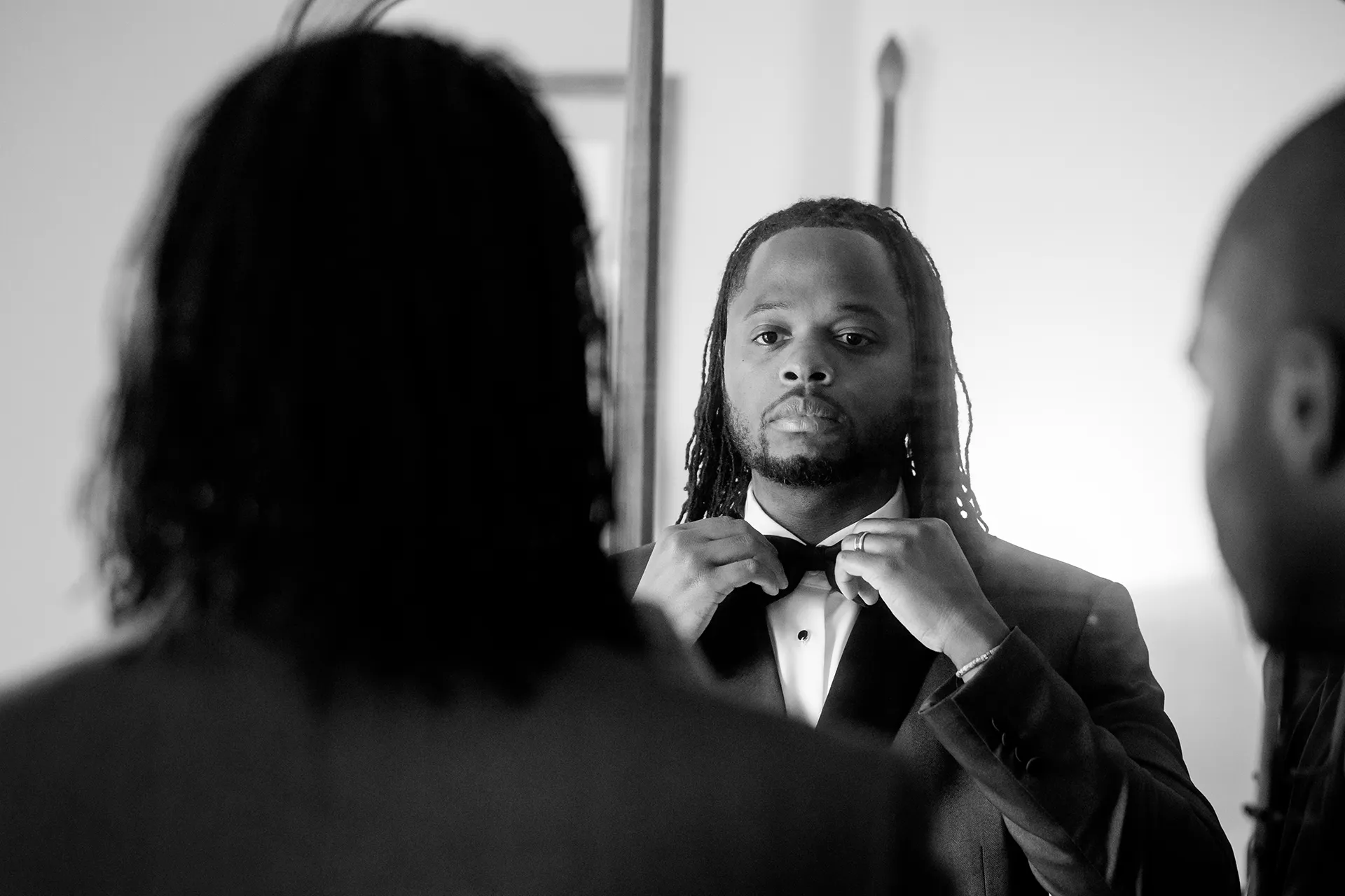 A groom adjusts his bowtie in a mirror as he gets ready for a wedding in Bangor, Maine.