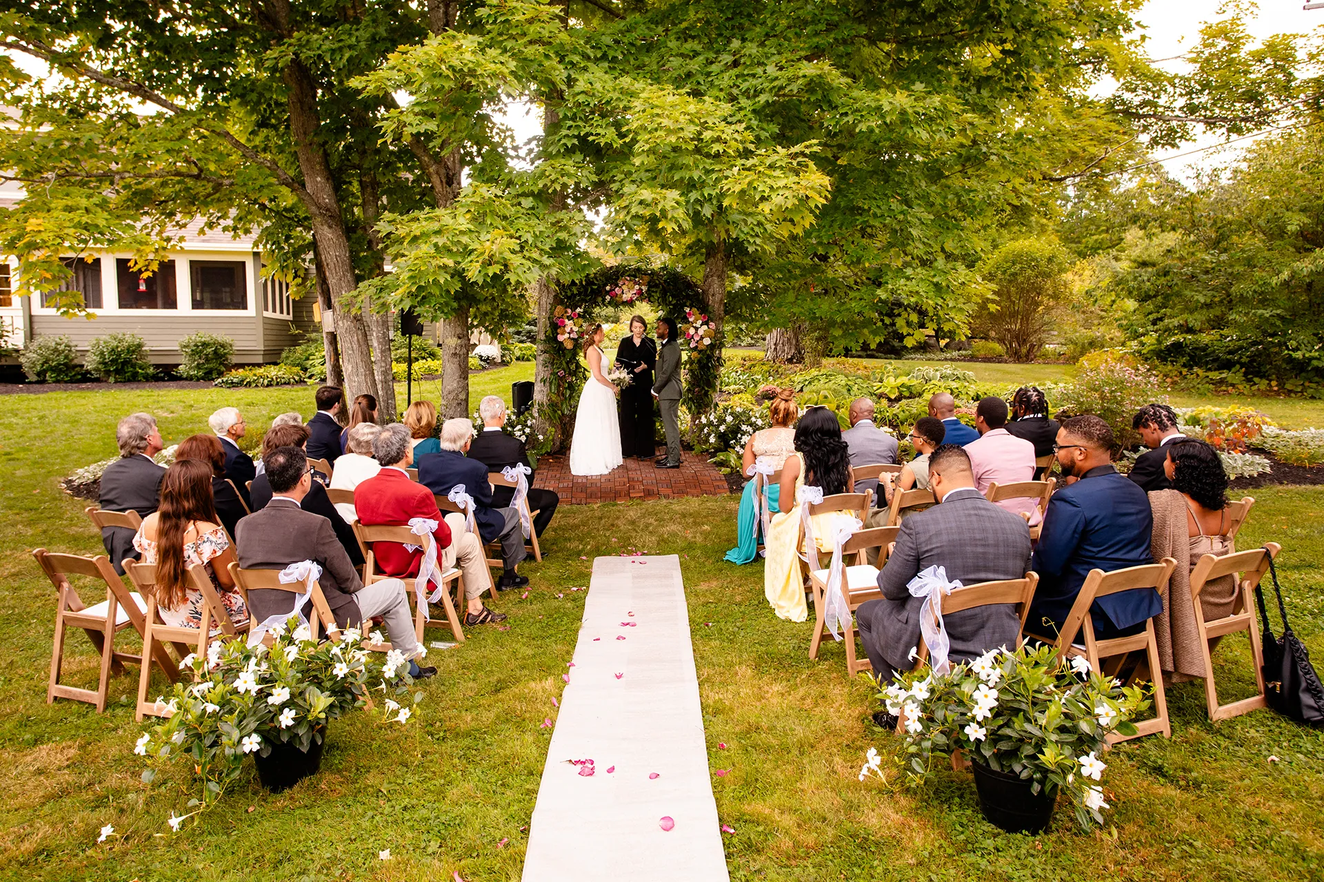 A bride and groom stand in front of a flower arbor during a micro wedding ceremony in Bangor, Maine.