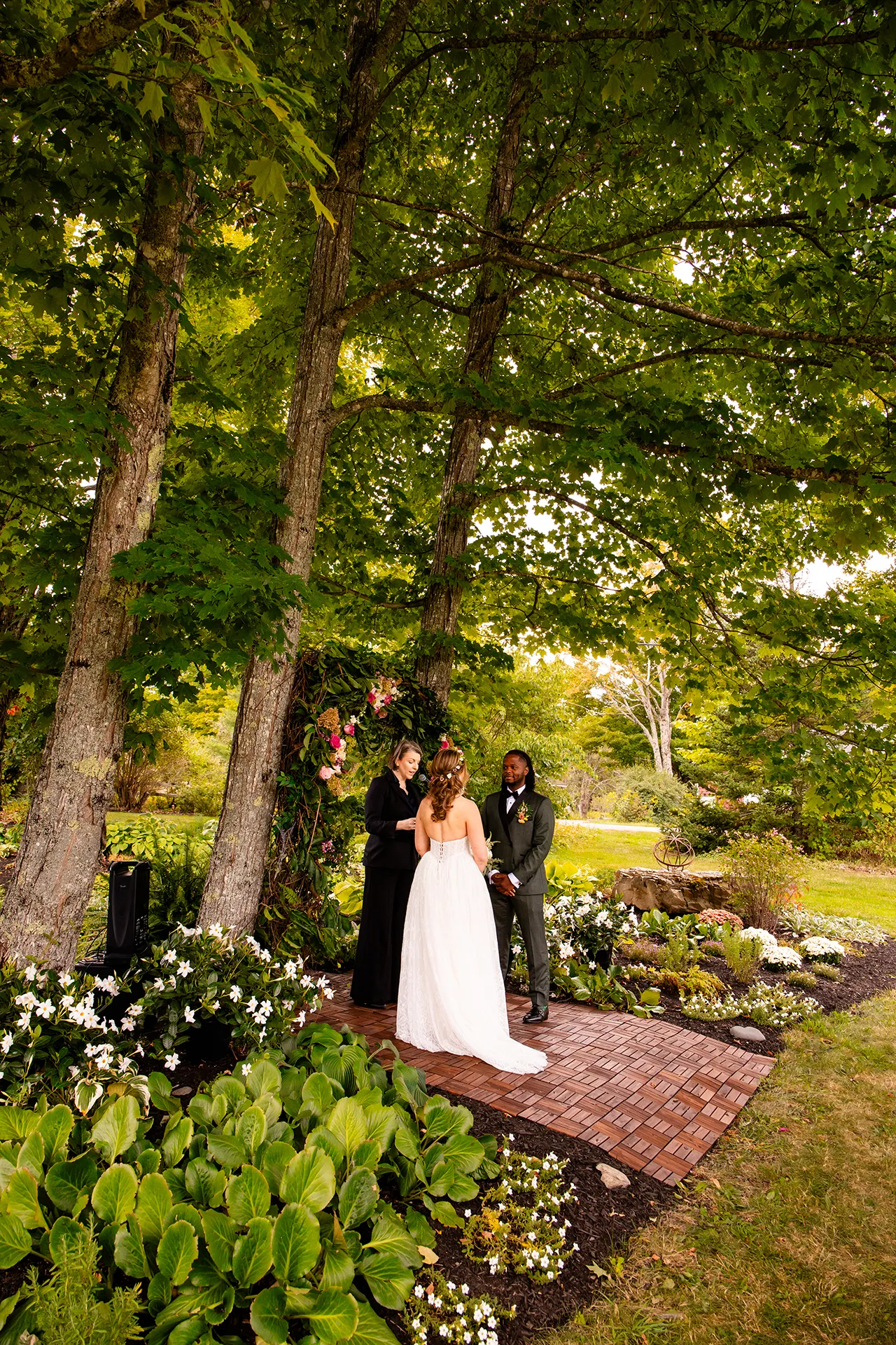 A couple stands in a garden in front of a flower arbor during a wedding ceremony in Bangor, Maine.