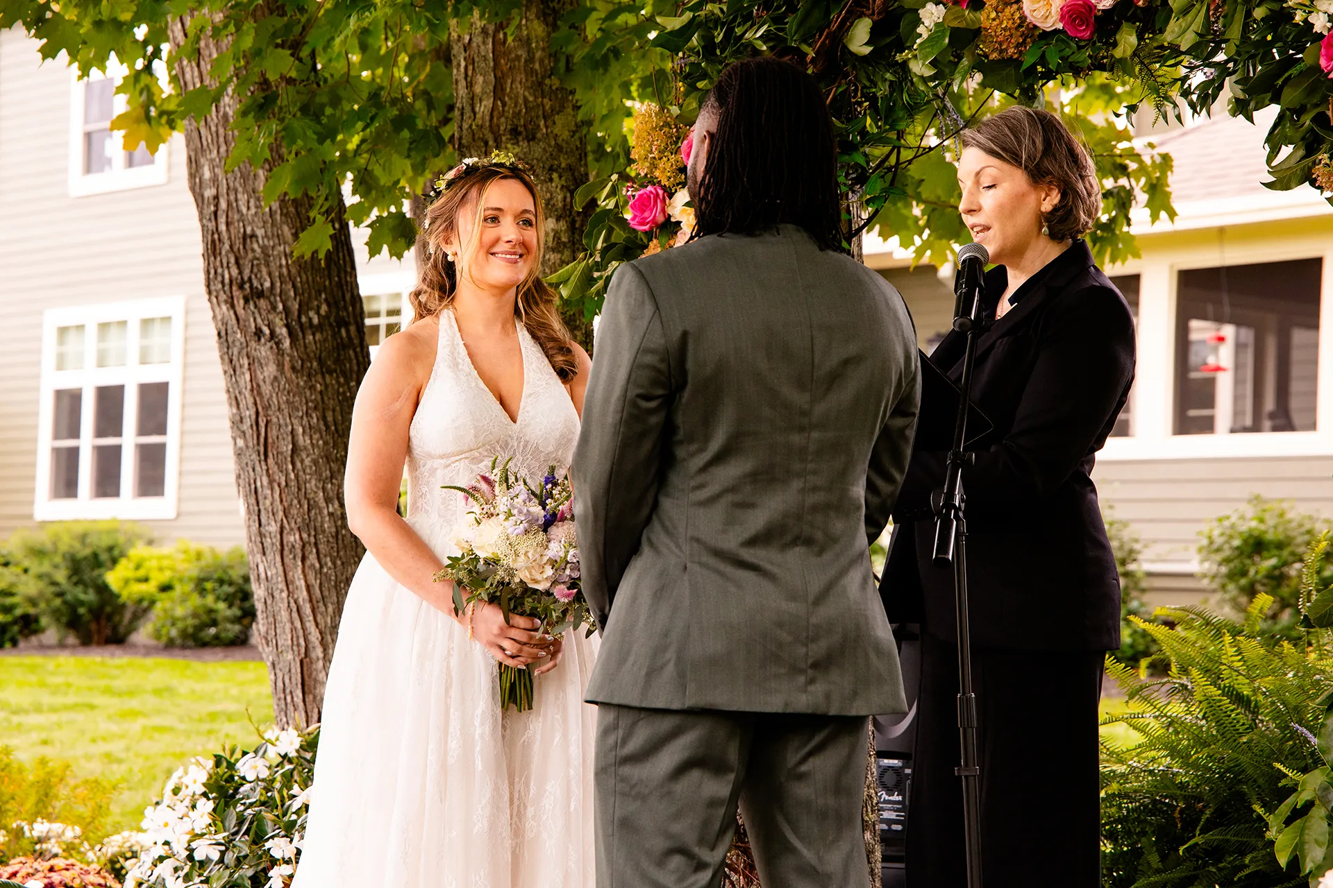 A bride smiles at a groom in front of a flower arbor during a wedding ceremony in Bangor, Maine.