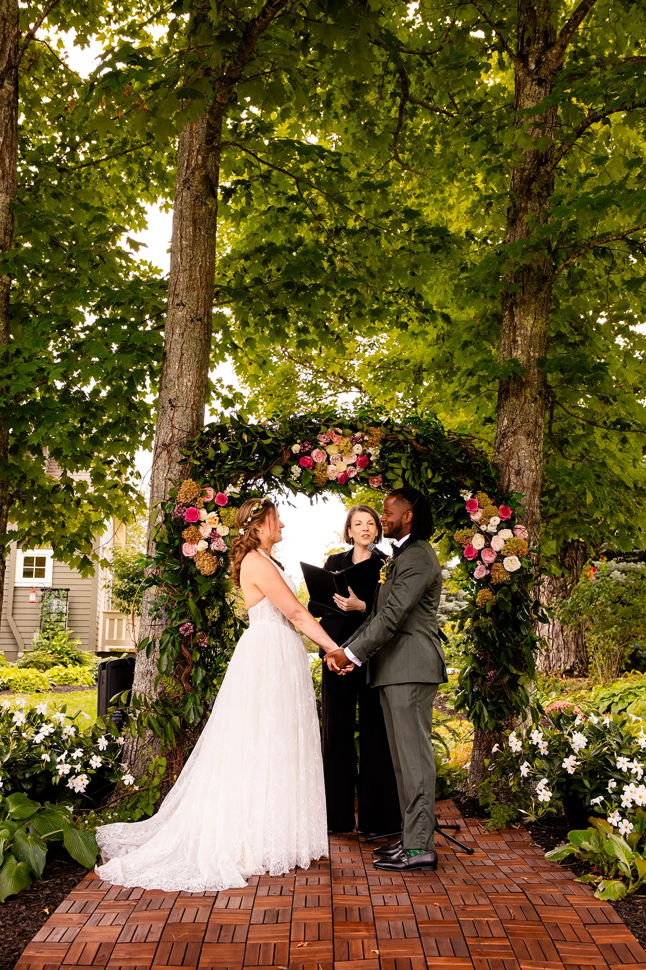 A bride and groom hold hands in front of a flower arbor during a wedding ceremony in Bangor, Maine.