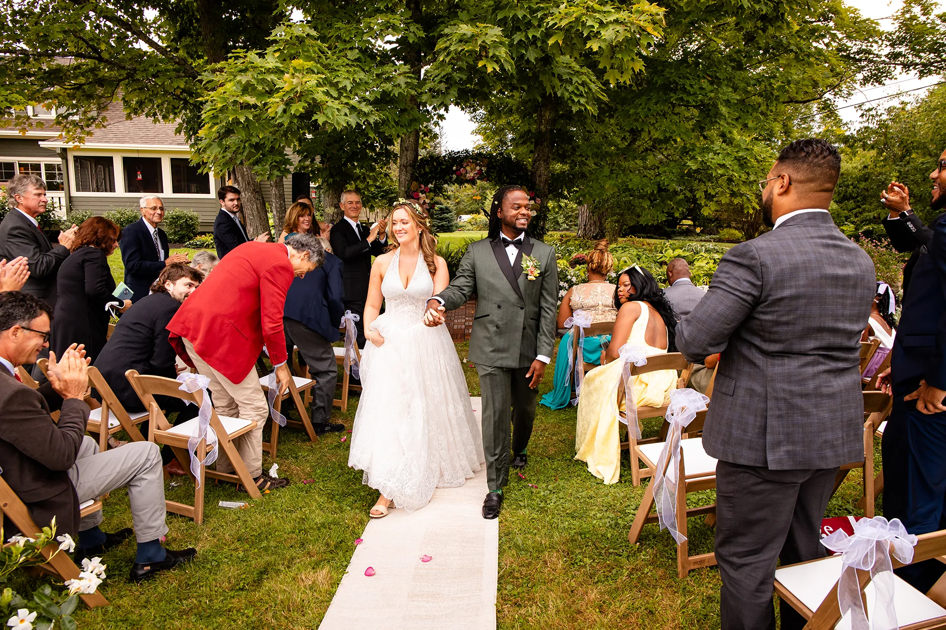 A bride and groom hold hands and walk down an aisle as guests clap during a wedding ceremony in Bangor, Maine.