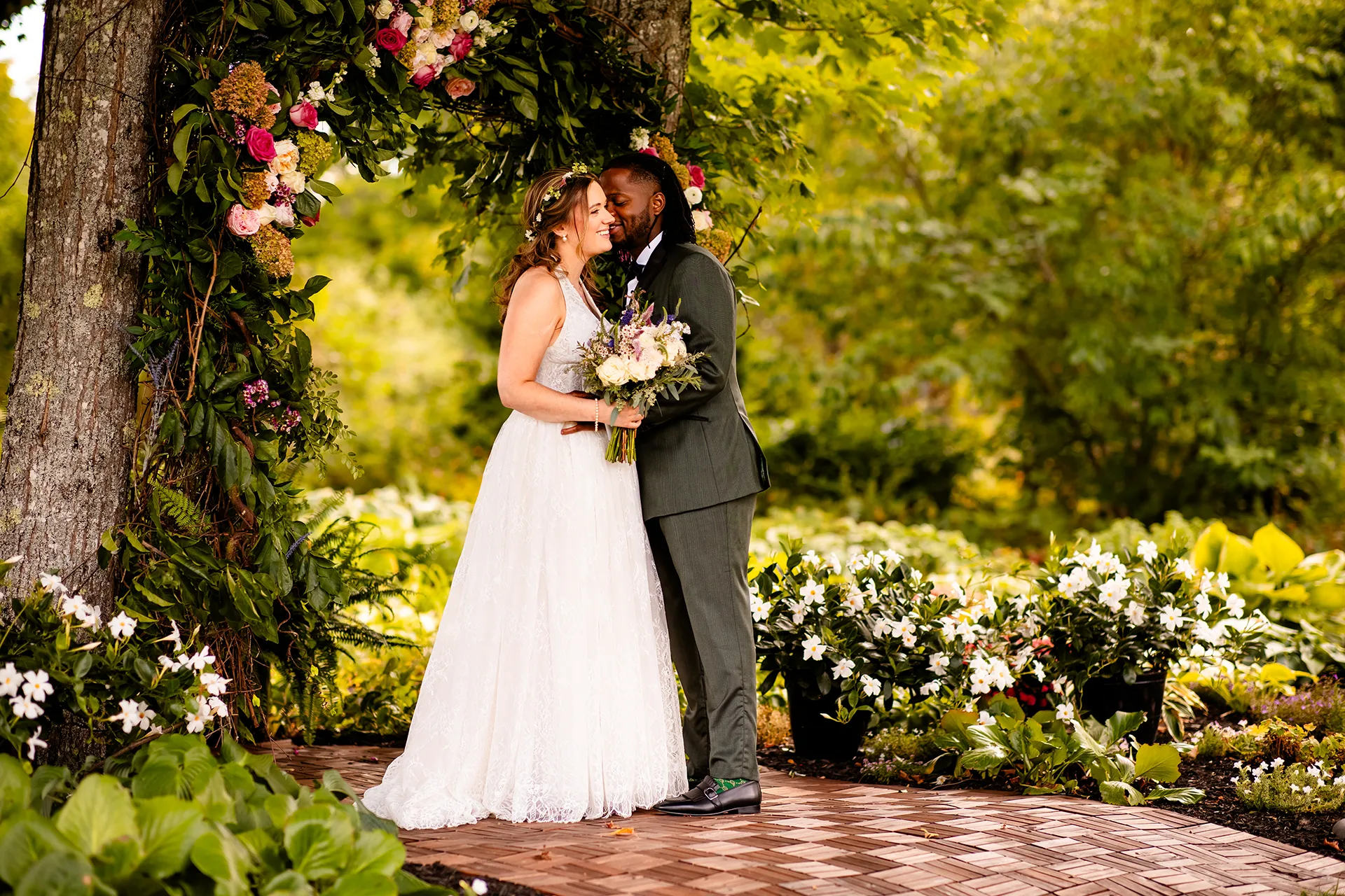A recently married couple laugh together in a garden during wedding portraits in Bangor, Maine.
