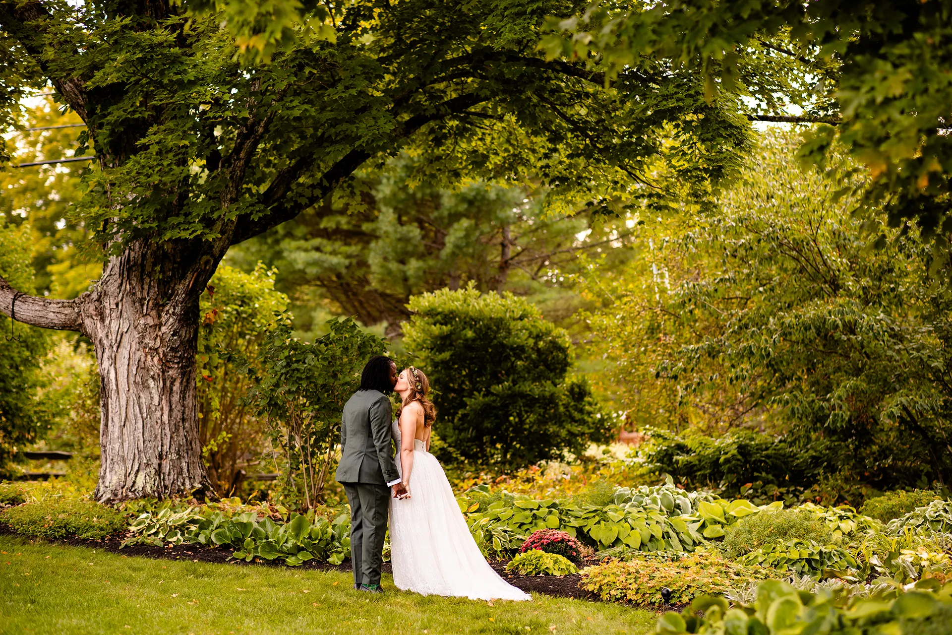 A bride and groom hold hands and kiss in a garden during wedding portraits in Bangor, Maine.