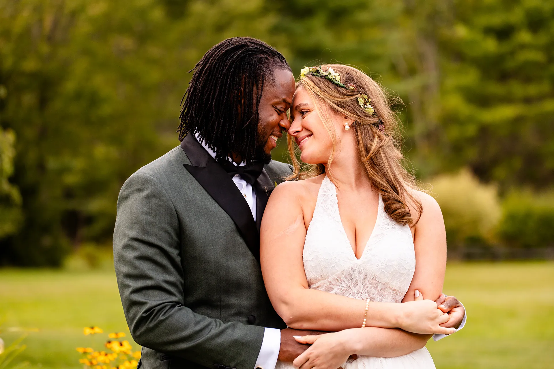 A bride and groom smile as they wrap their arms around each other during wedding portraits in Bangor, Maine.