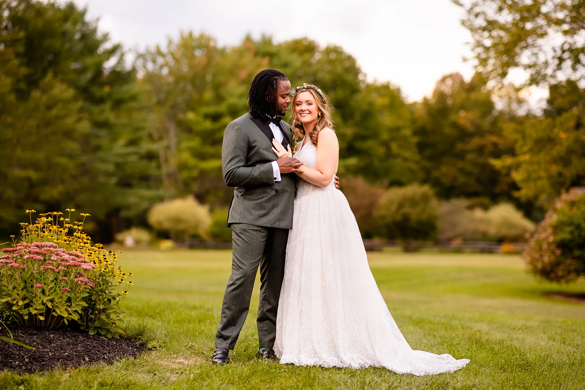 A groom looks at a smiling bride while they hold hands during wedding portraits in Bangor, Maine.