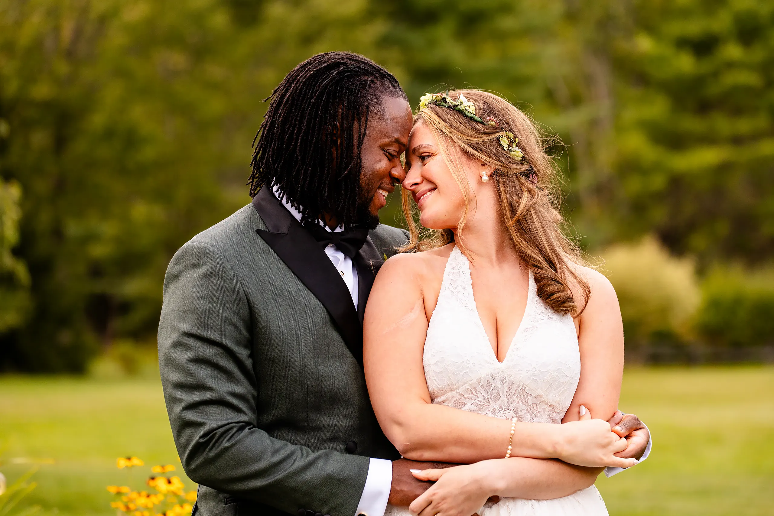 A bride and groom smile as they wrap their arms around each other during wedding portraits in Bangor, Maine.