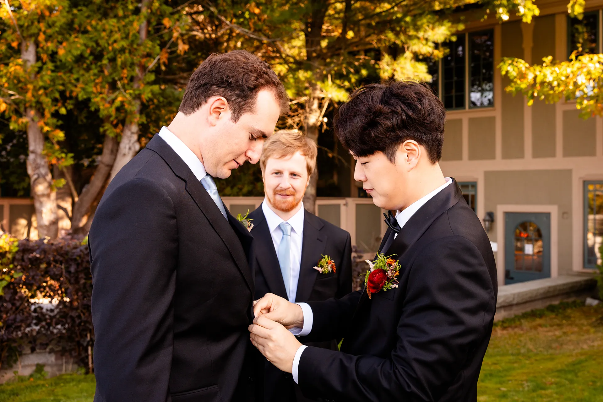 A groom helps a groomsman button his jacket as they get ready for a wedding at the Bar Harbor Club near Acadia National Park in Maine.