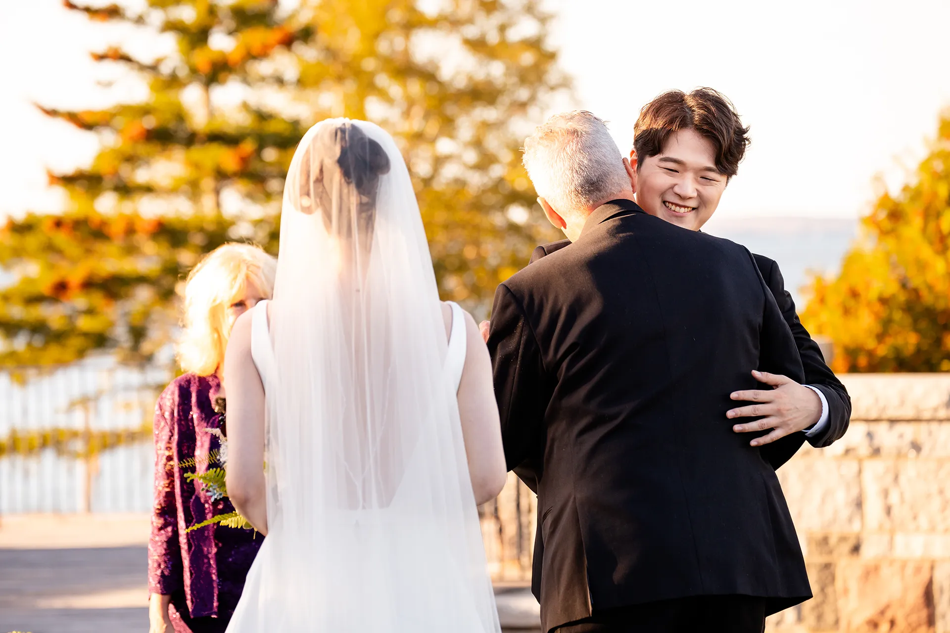 A dad hugs a smiling groom during a wedding ceremony at the Bar Harbor Club near Acadia National Park in Maine.