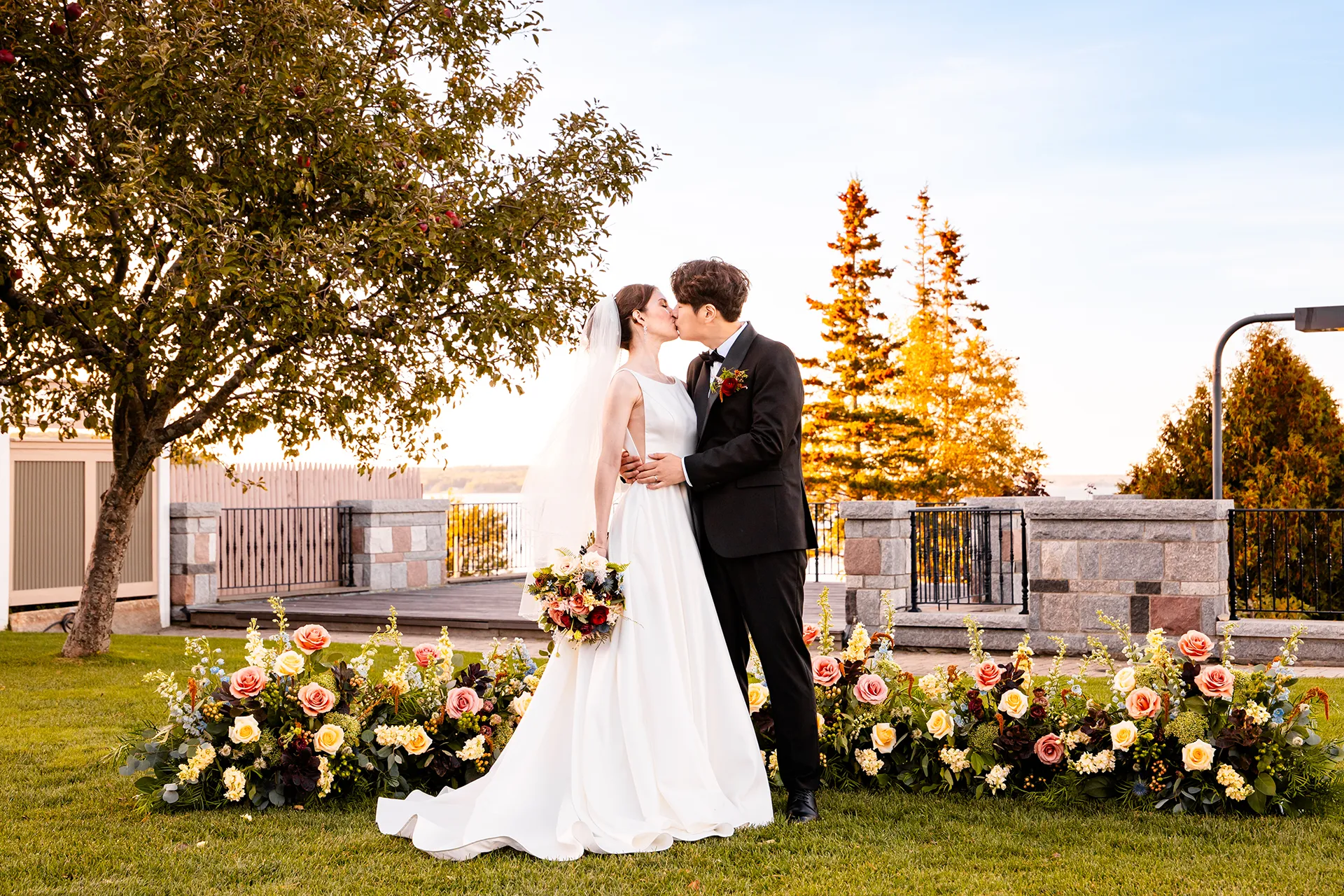 A newly married couple kiss in front of flowers during wedding portraits at the Bar Harbor Club near Acadia National Park in Maine.