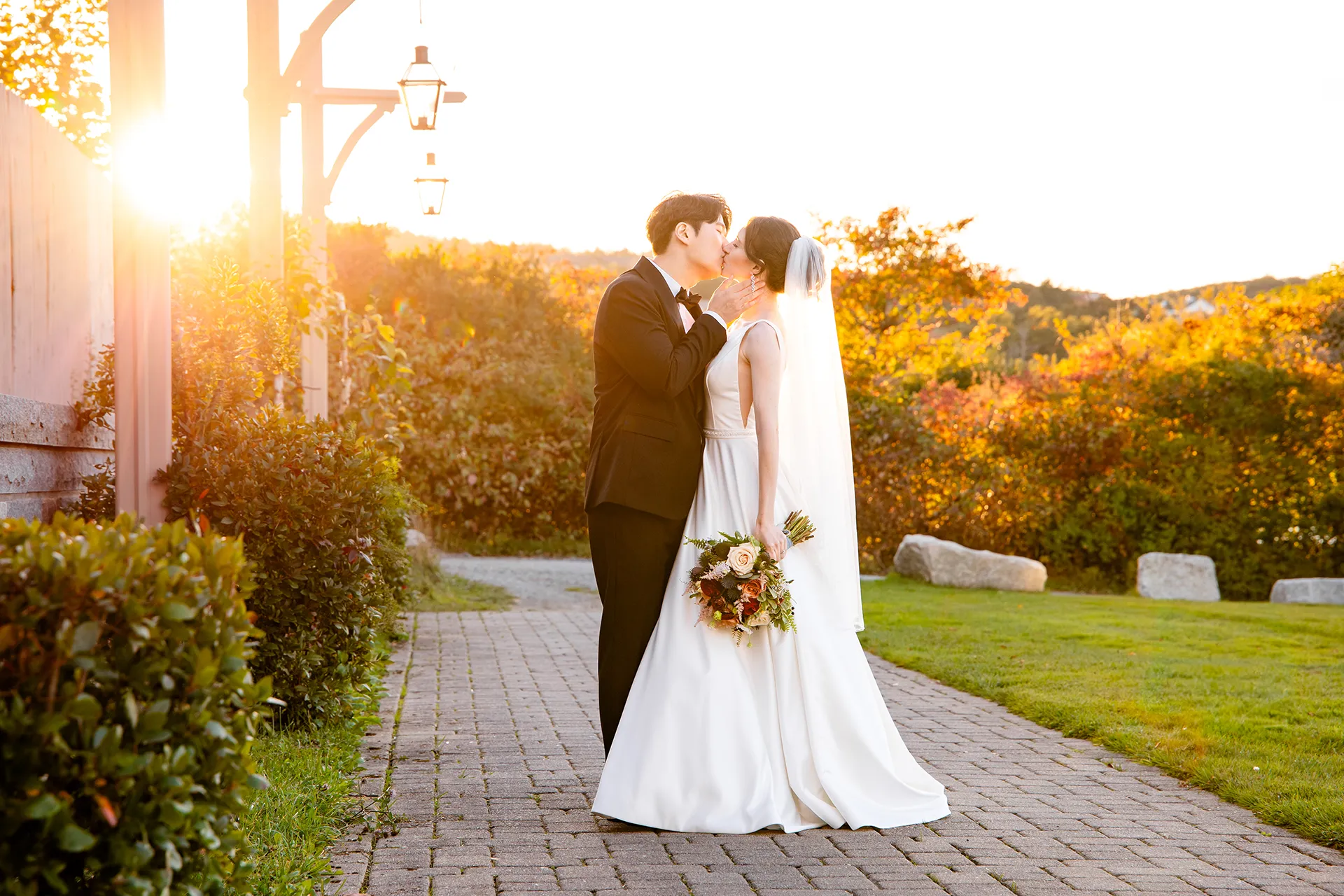 A bride and groom kiss as the sun shines behind them during wedding portraits at the Bar Harbor Club near Acadia National Park in Maine.