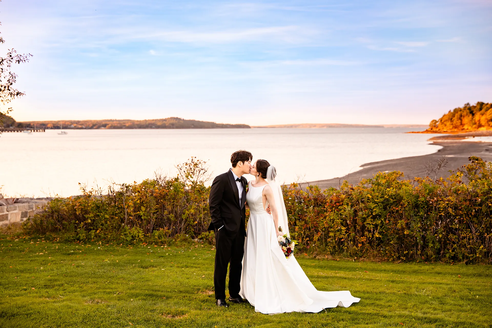 A bride and groom kiss in front of Frenchman Bay during wedding portraits at the Bar Harbor Club near Acadia National Park in Maine.