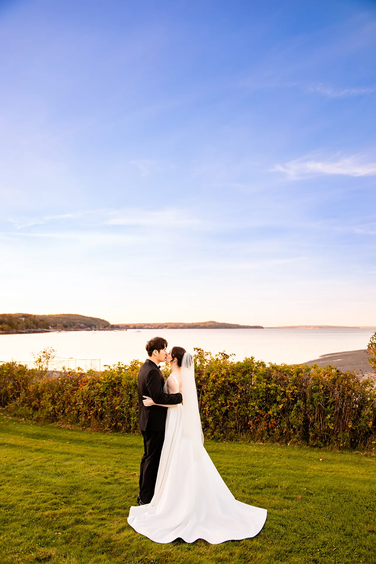 A recently married couple kiss in front of Frenchman Bay during wedding portraits at the Bar Harbor Club near Acadia National Park in Maine.