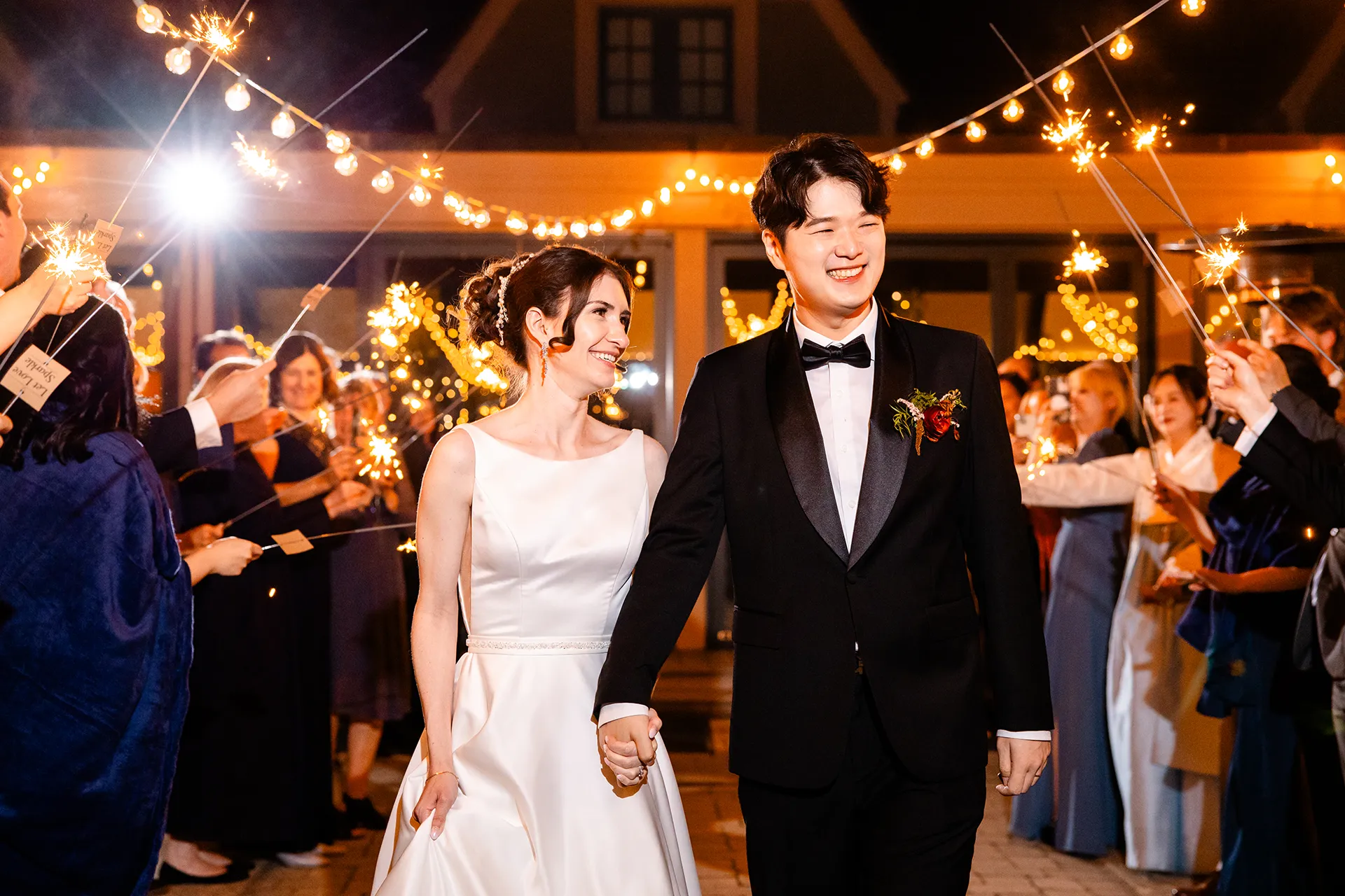 A bride and groom hold hands as they walk by their guests holding sparklers during a wedding reception at the Bar Harbor Club in Maine.