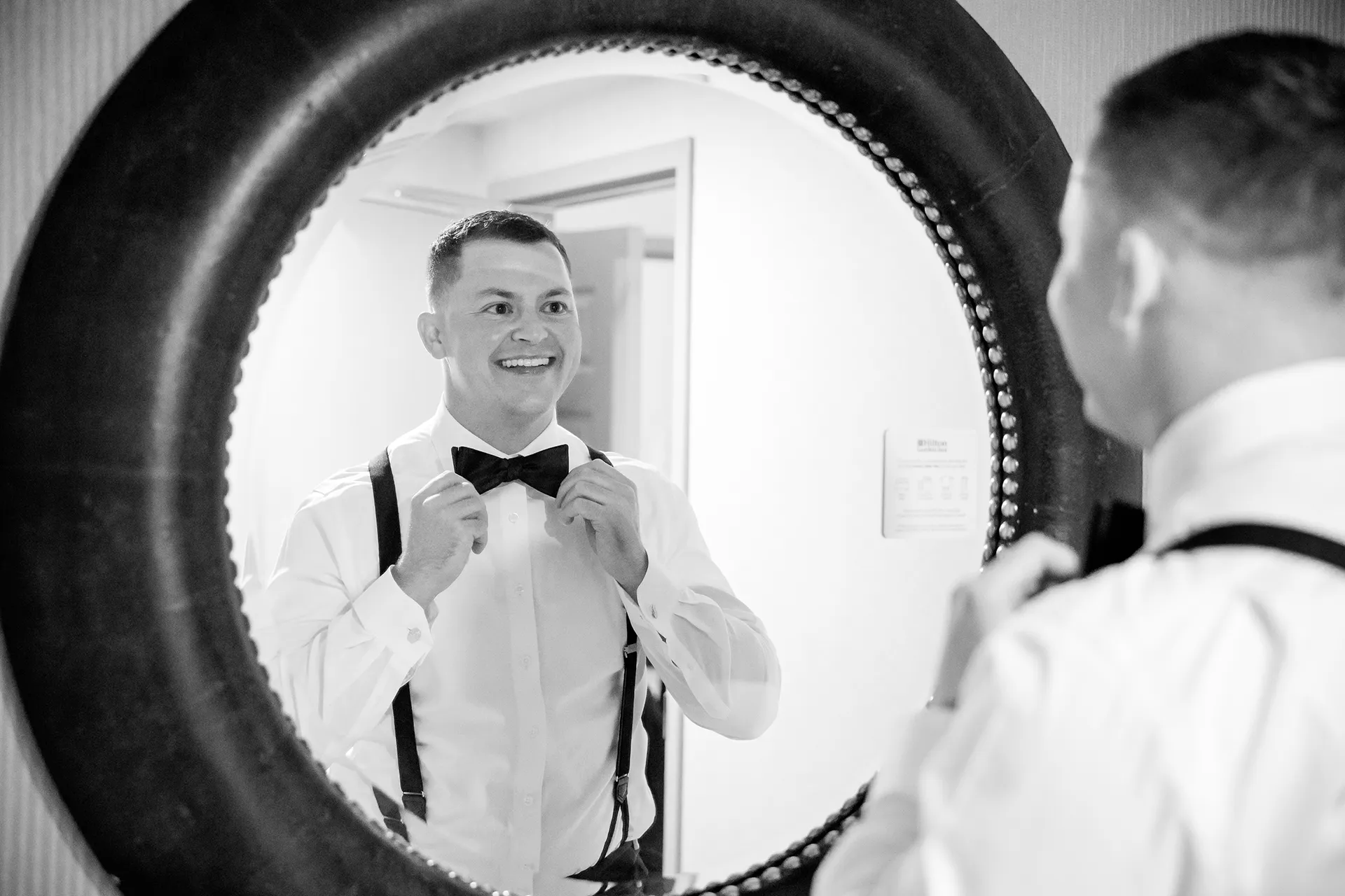 A groom adjusts his bowtie in a mirror as he gets ready for a wedding at Fruitlands Museum in Harvard Massachusetts.