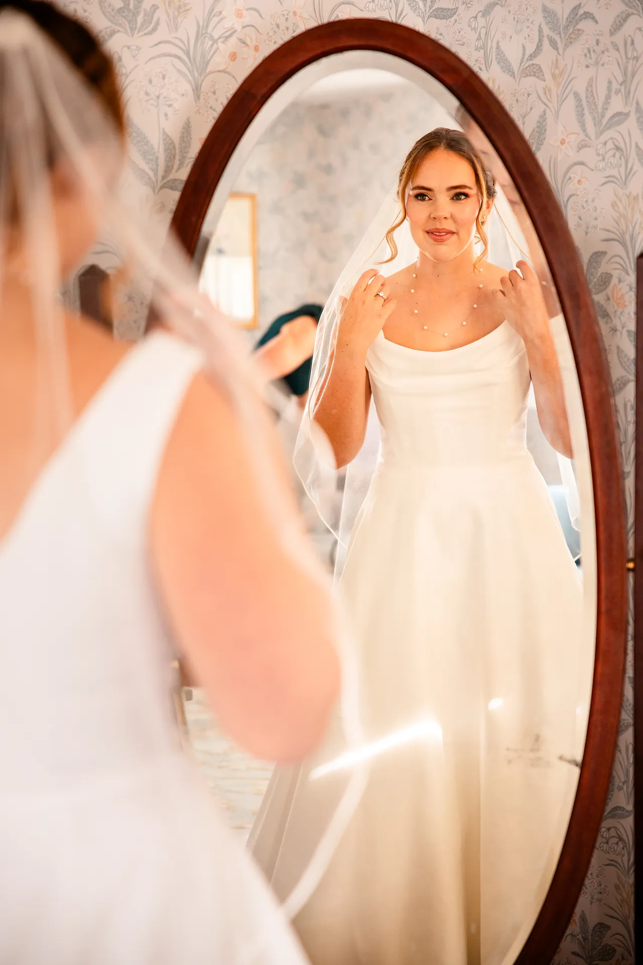 A bride looks at herself in the mirror as she gets ready for a wedding at Fruitlands Museum in Harvard Massachusetts.