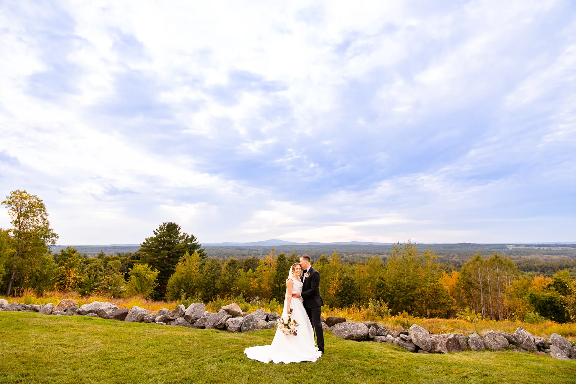 A groom kisses a smiling bride on the head during wedding portraits at Fruitlands Museum in Harvard, Massachusetts.